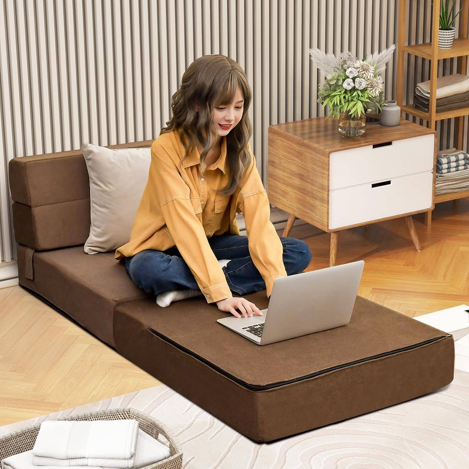 Frau sitzt auf einem ausklappbaren Sofa-Bett und benutzt einen Laptop in einem ordentlichen Wohnzimmer mit einem Beistelltisch und Blumen.