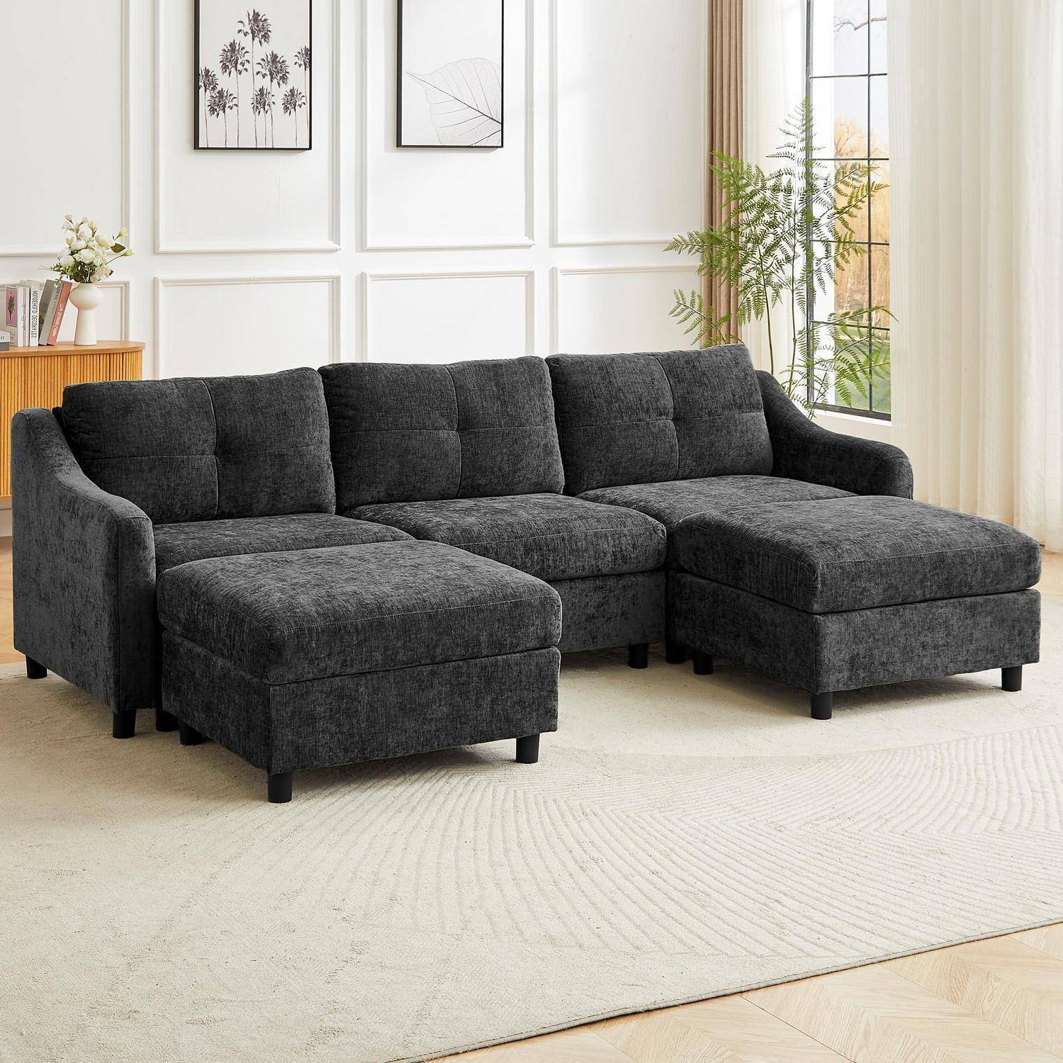 Dunkelgraues modulares Sektionalsofa mit Chaiselongue in einem hellen Wohnzimmer, auf einem hellen Teppich neben Fenstern und Wandkunst dargestellt.