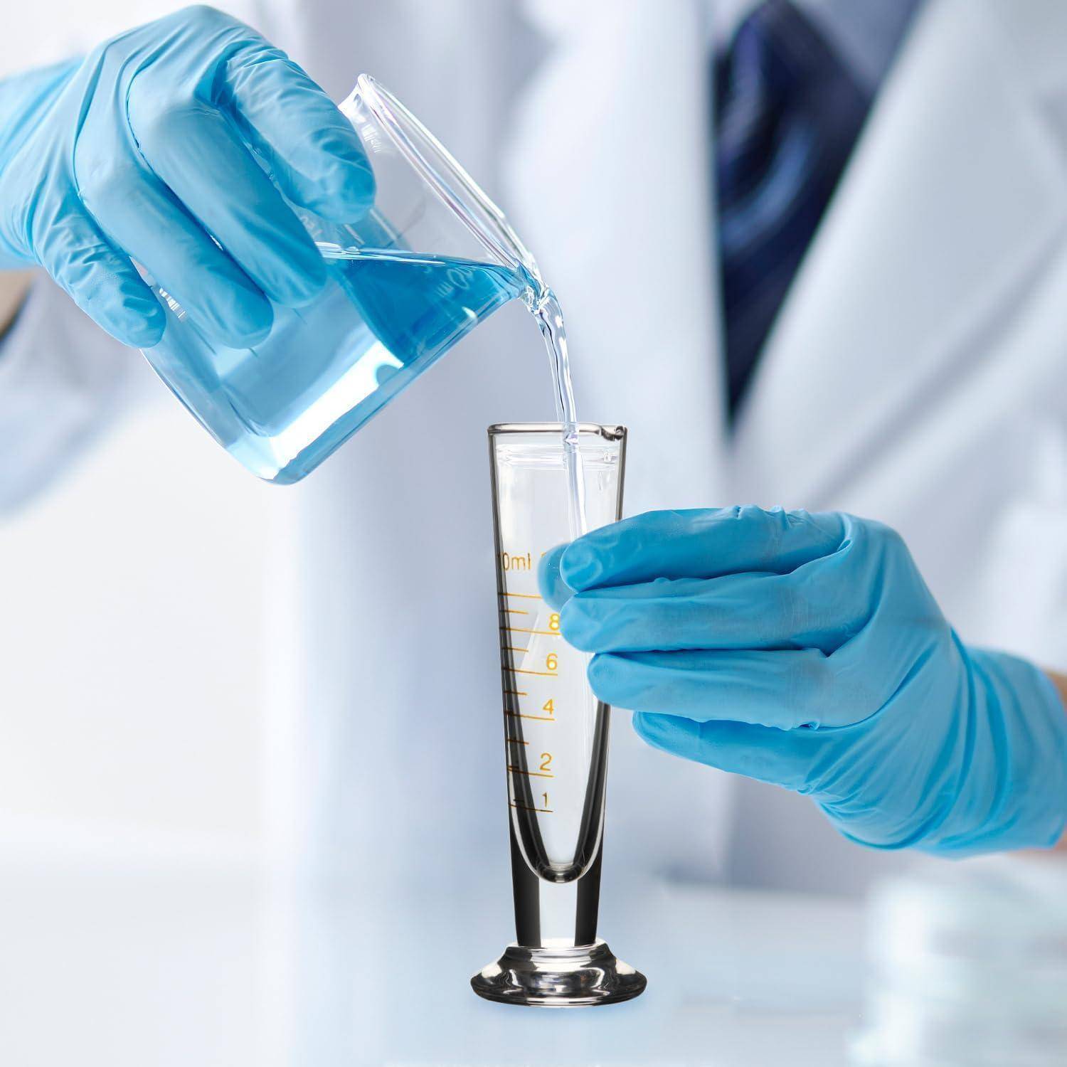 Wissenschaftler mit Handschuhen gießt blaue Flüssigkeit aus einem Becherglas in einen Messzylinder in einer Labornahaufnahme.