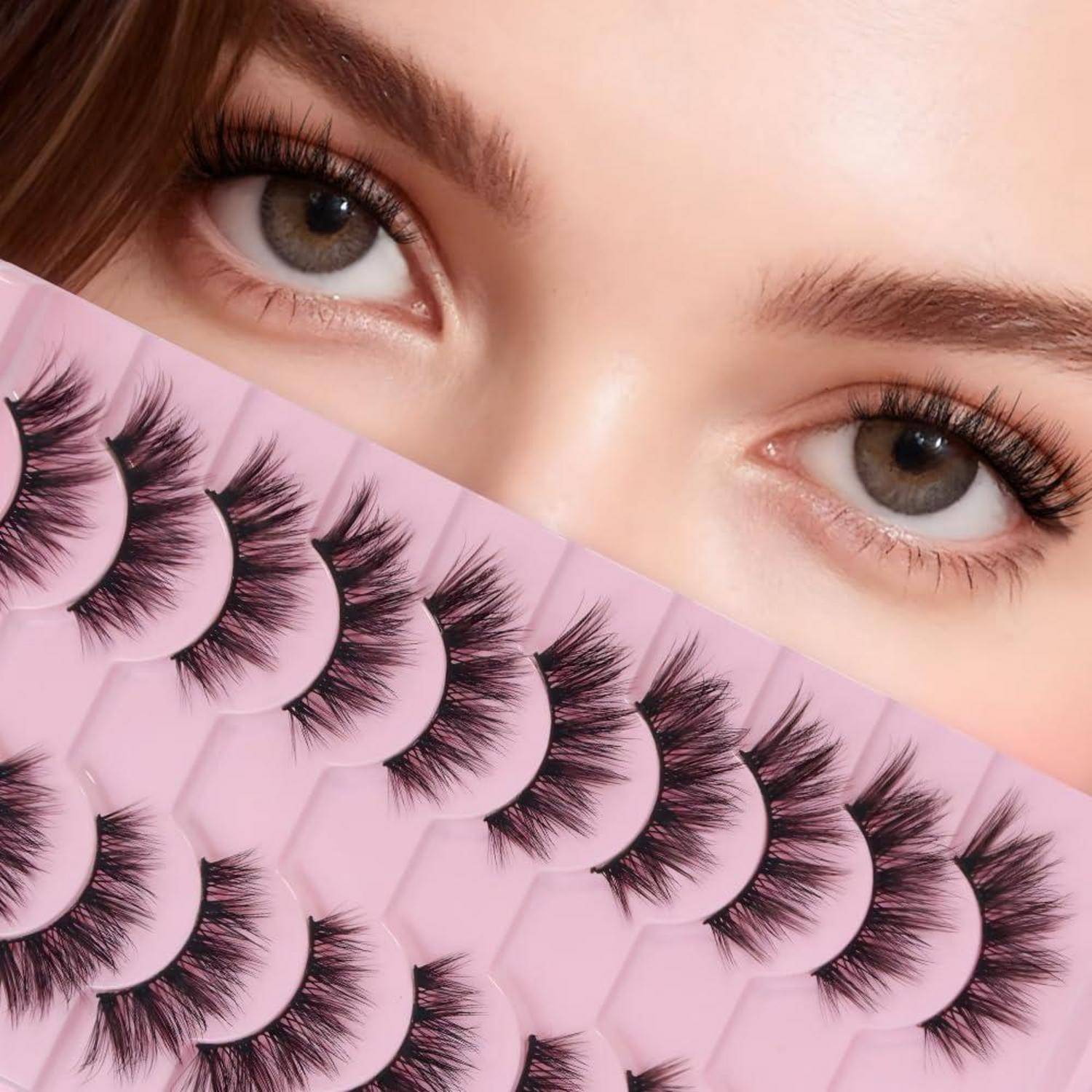 Nahaufnahme der Augen einer Frau über einer Auswahl von künstlichen Wimpern auf rosa Hintergrund, was auf eine Schönheits- oder Kosmetikwerbung hindeutet.