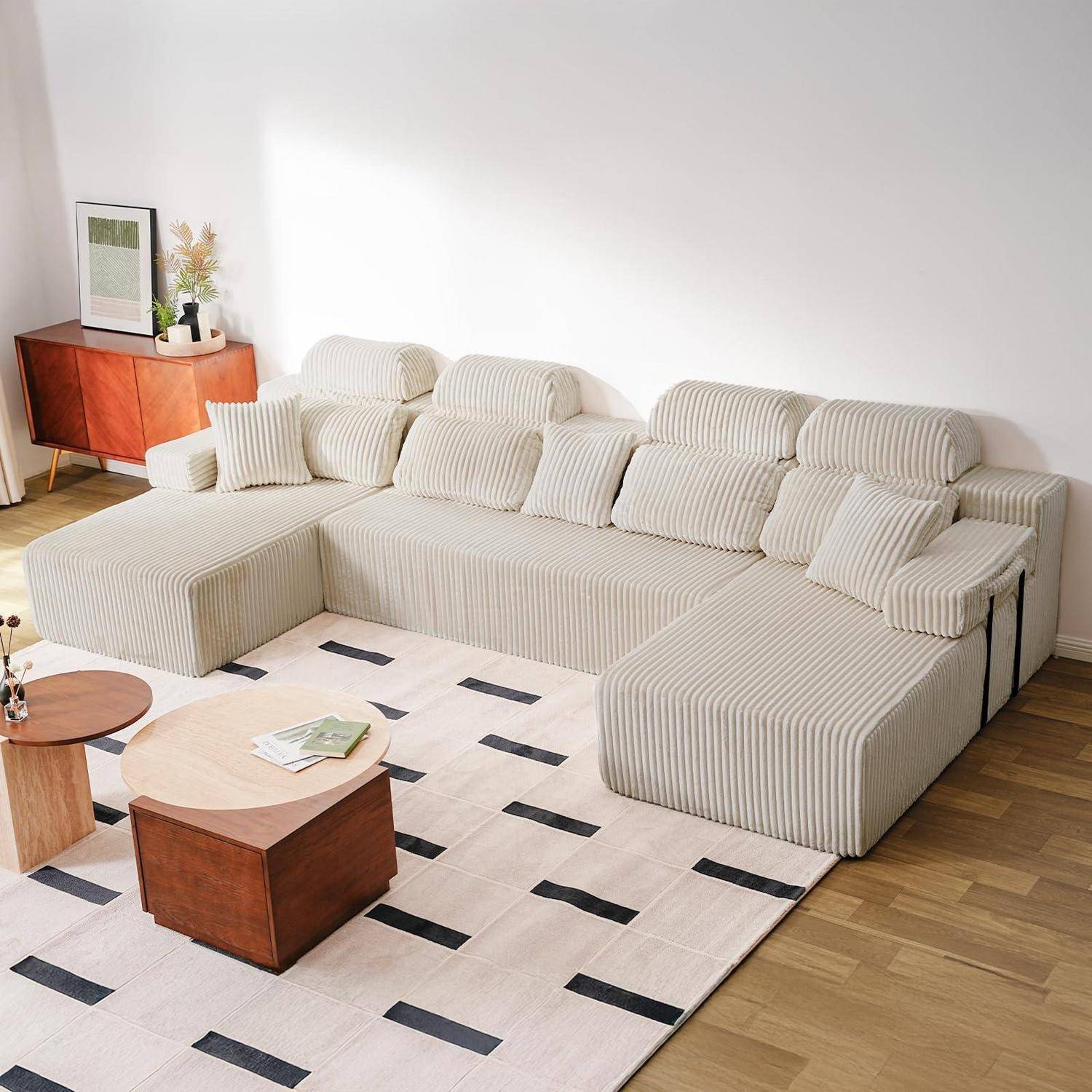 Modernes Wohnzimmer mit großem gestreiftem Ecksofa, passenden Kissen, hölzernem Sideboard und geometrischem Teppich auf hellem Holzboden.