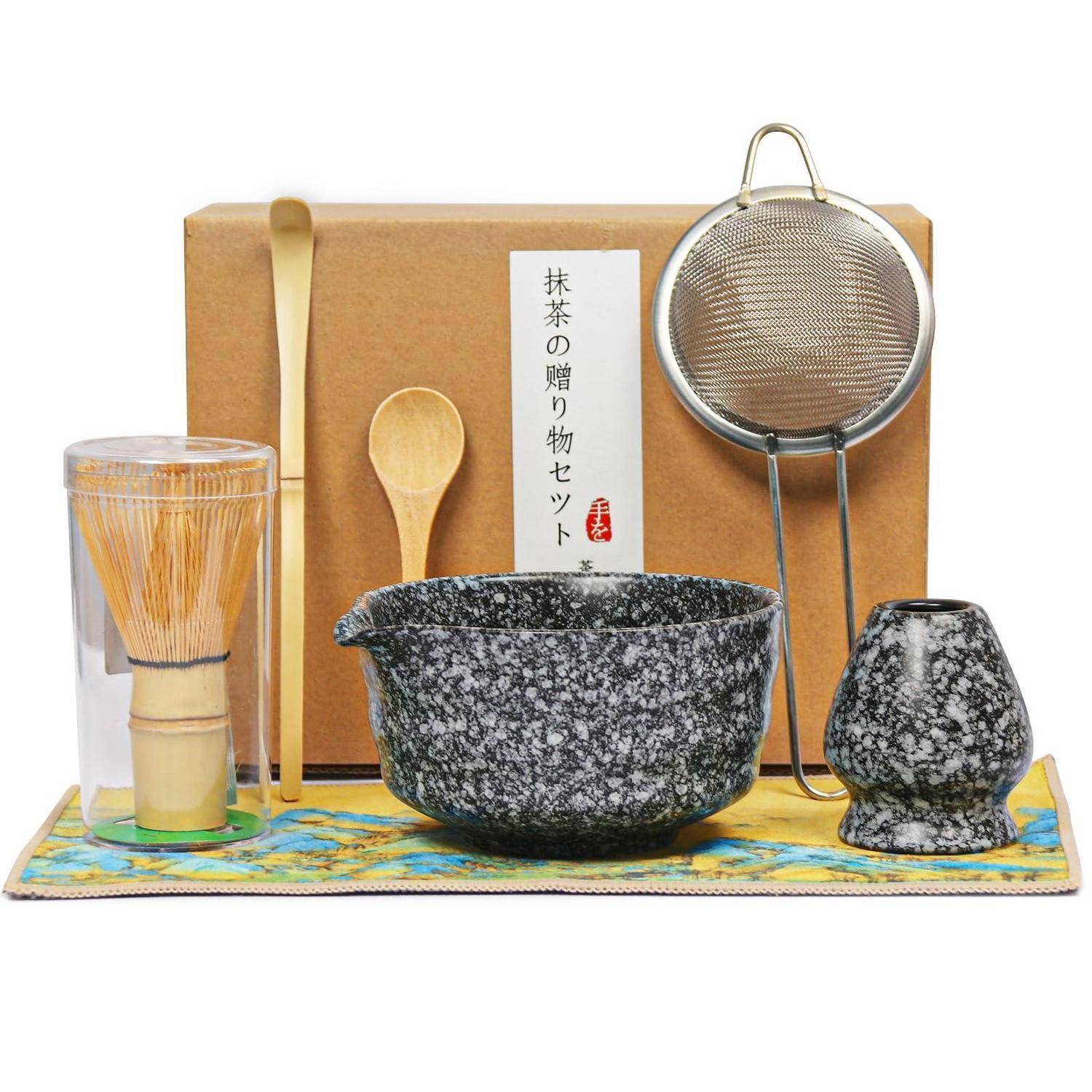 Matcha-Tee-Zeremonieset mit Schüssel, Schneebesen, Löffel, Schaufel, Sieb und kleiner Tasse, angeordnet vor einer beschrifteten Schachtel auf einem Tuch.