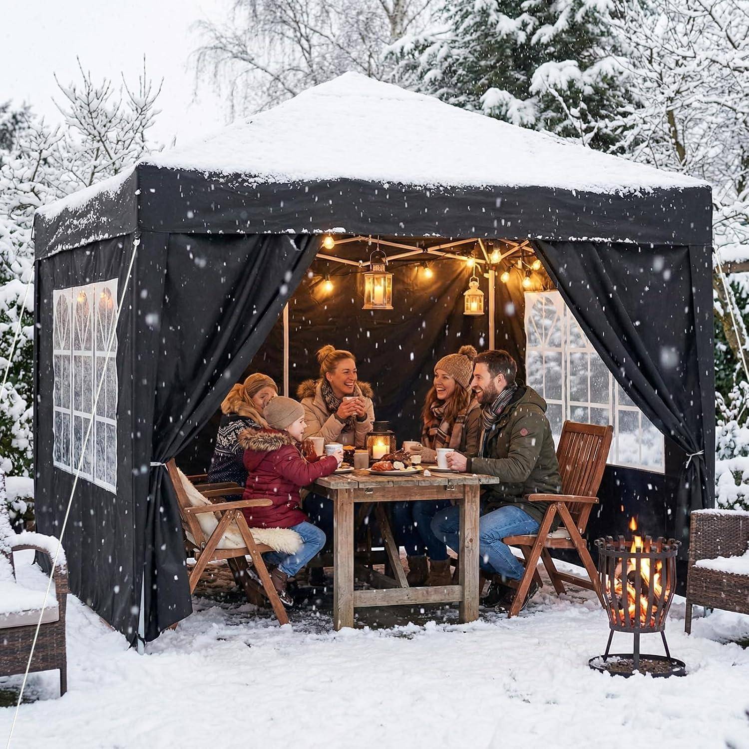 Eine Familie sitzt um einen Tisch in einem schneebedeckten Außenzelt und teilt Getränke und Gespräche bei warmem Laternenlich und einem Feuerplatz.