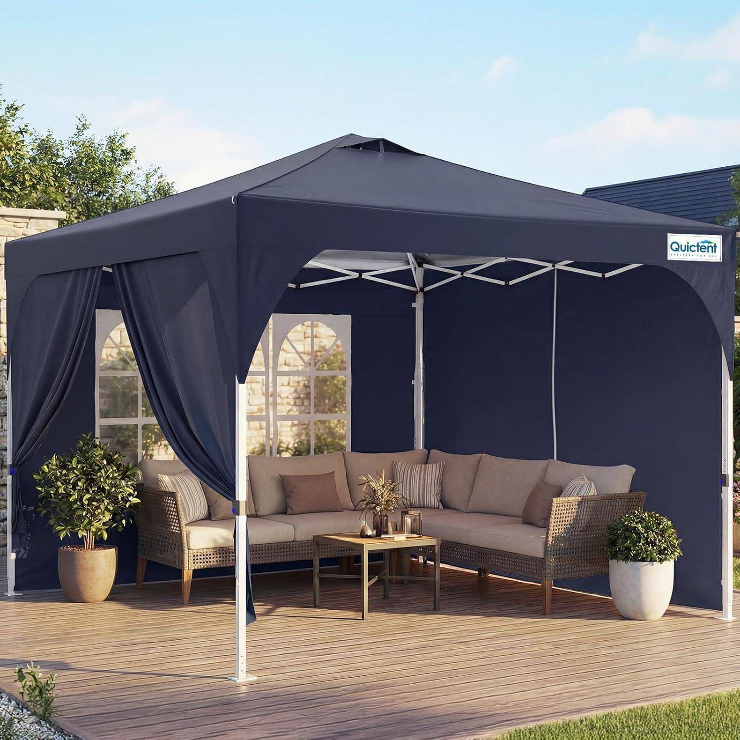 Dunkelblauer Außenpavillon mit Markise und Vorhängen über einem Korbsektional, Couchtisch und Topfpflanzen auf einer Holzterrasse