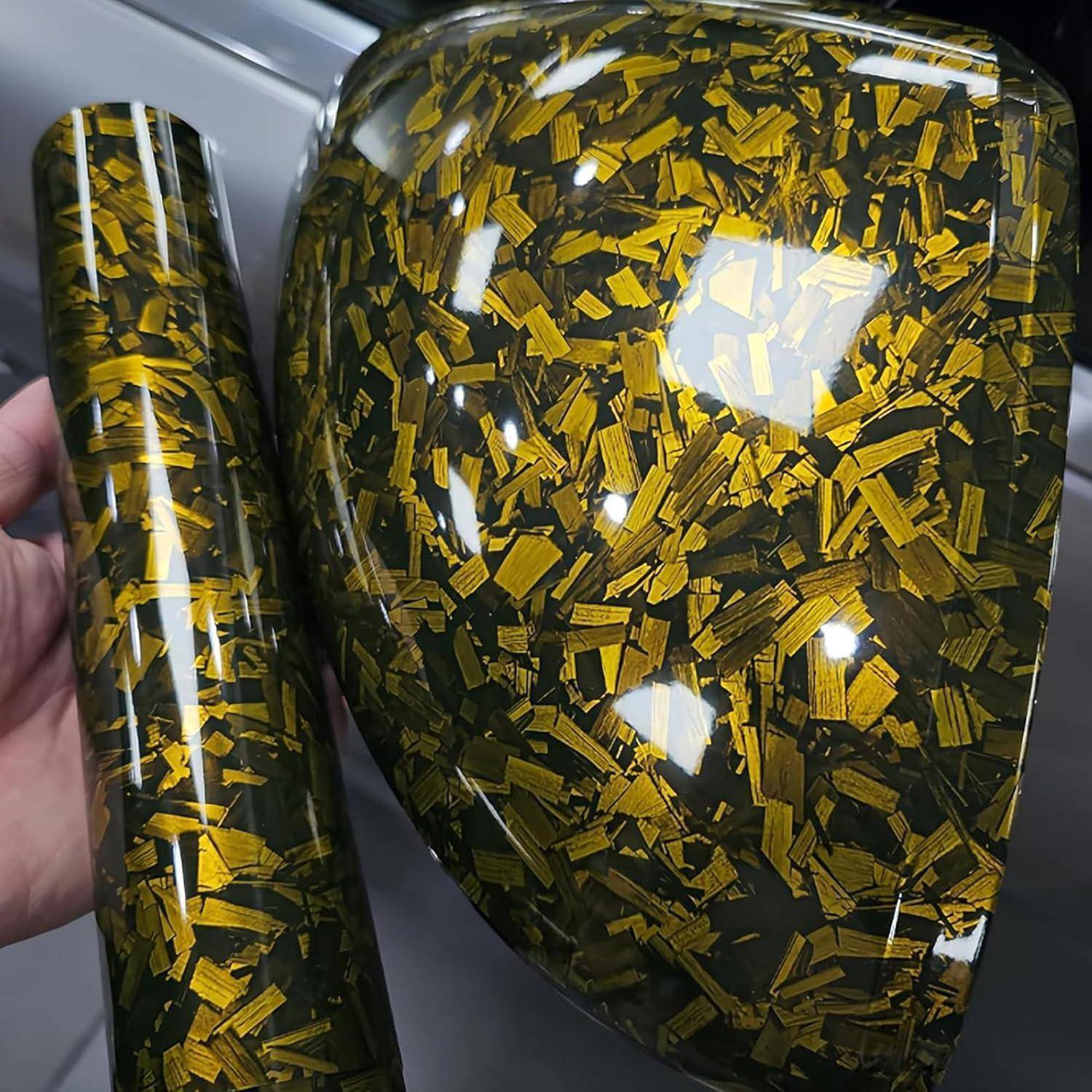 Zwei glänzende Harzteile mit Gold- und Schwarzflöckchen, ein großer gebogener Block und ein schmaler Zylinder, in einer Hand gehalten.