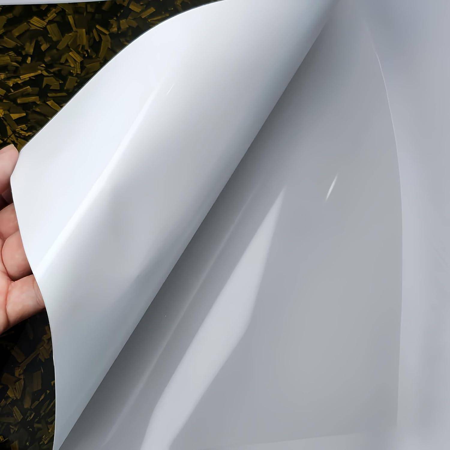 Nahaufnahme einer Hand, die ein leeres weißes Blatt oder Etikett zurückzieht und seine glänzende Unterseite gegen einen dunkel gemusterten Hintergrund enthüllt.