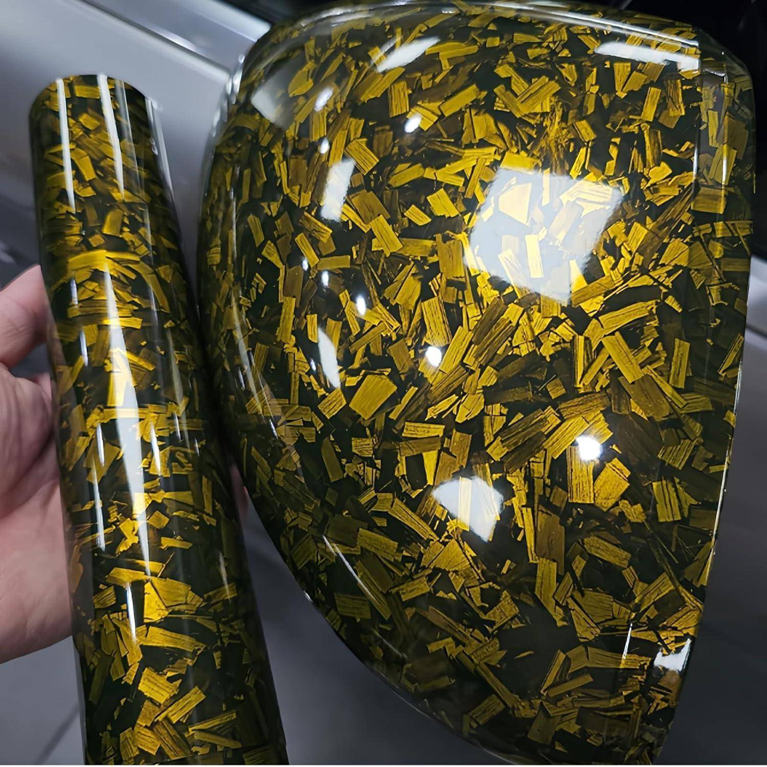 Nahaufnahme von zwei glänzenden dekorativen Zylindern oder Paneelen mit einem schwarzgoldenen konfettiähnlichen Muster, einer wird von einer Hand gehalten.