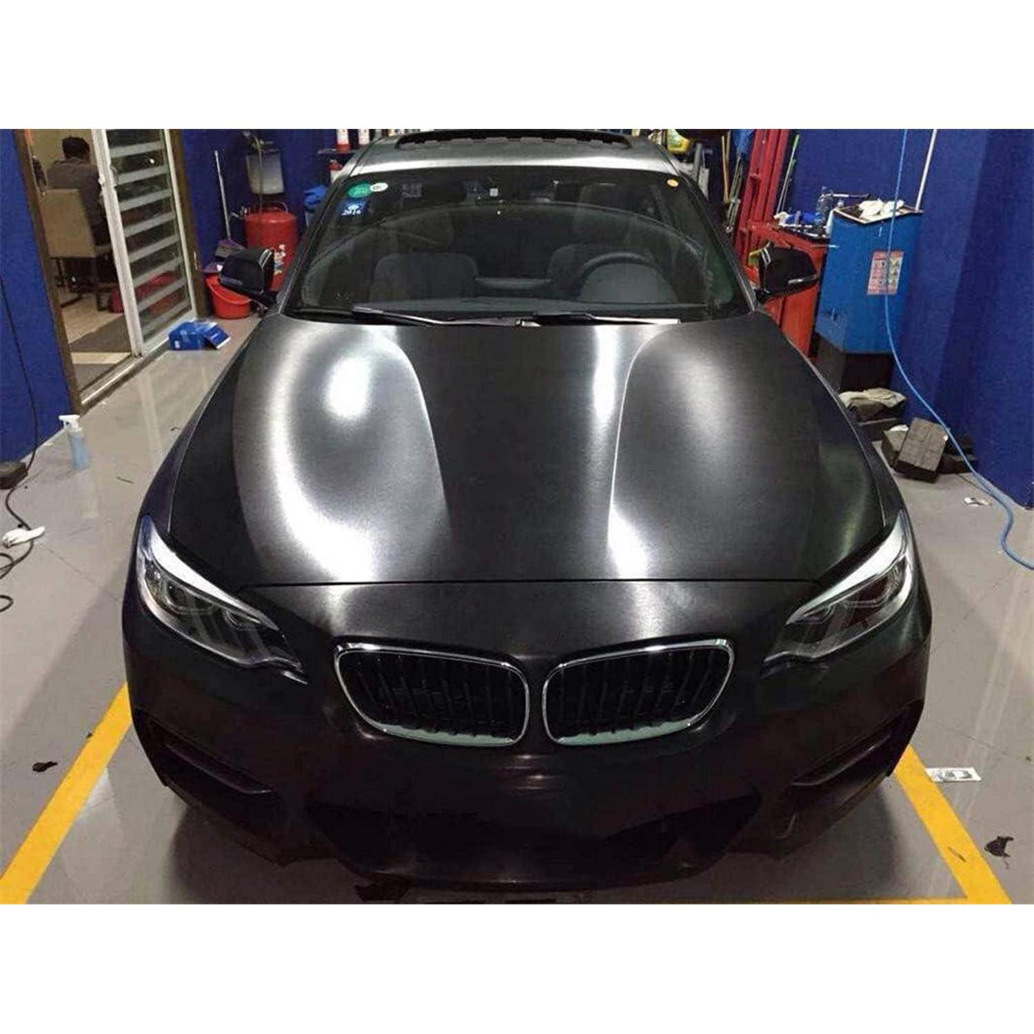 Schwarzer BMW Sedan mit matter Motorhaube und Dach, geparkt in einer Garage oder Autowerkstatt.