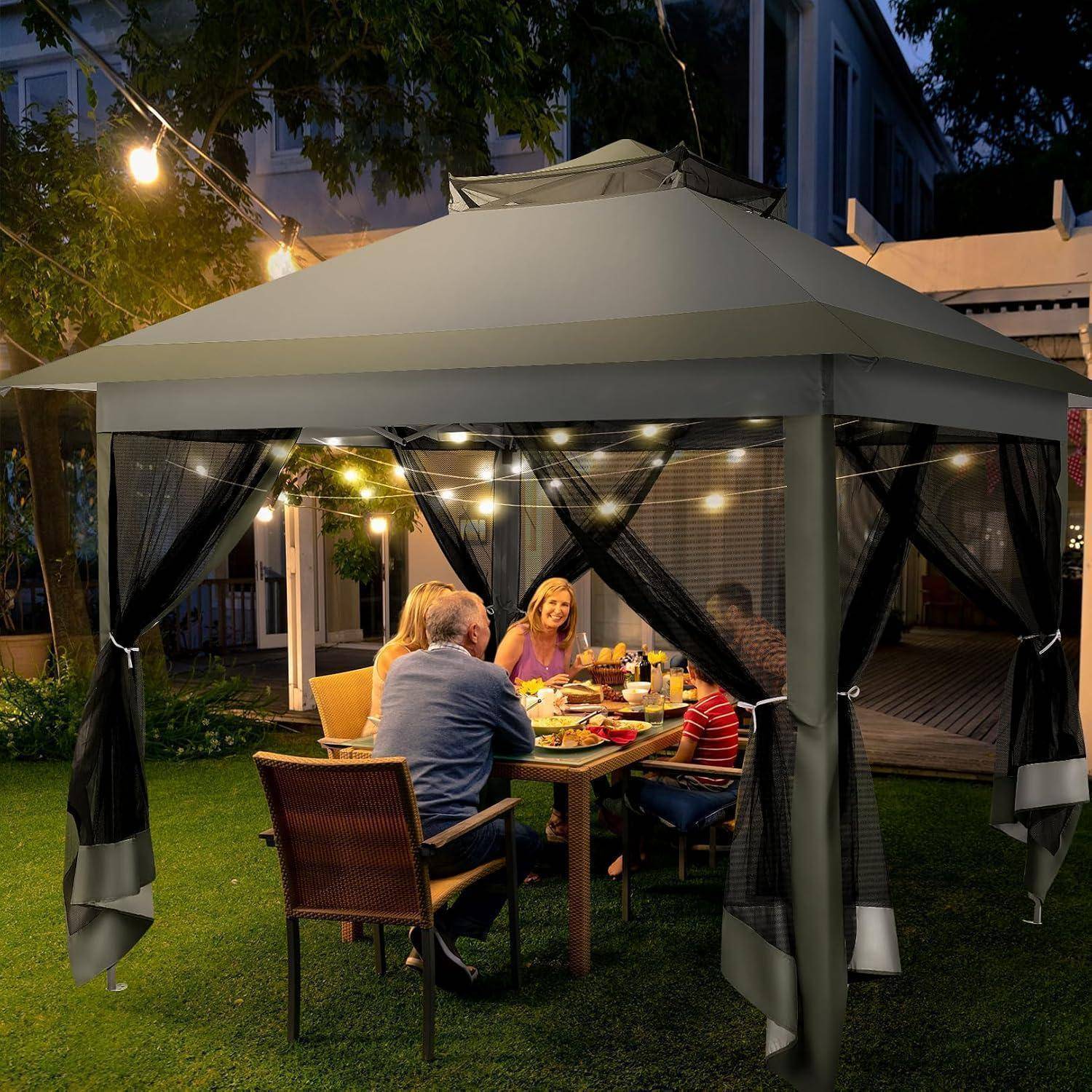 Familie sitzt unter einer beleuchteten Außenlaube nachts, vier Personen sitzen um einen Tisch in einem Garten oder Hinterhof herum beim Essen.