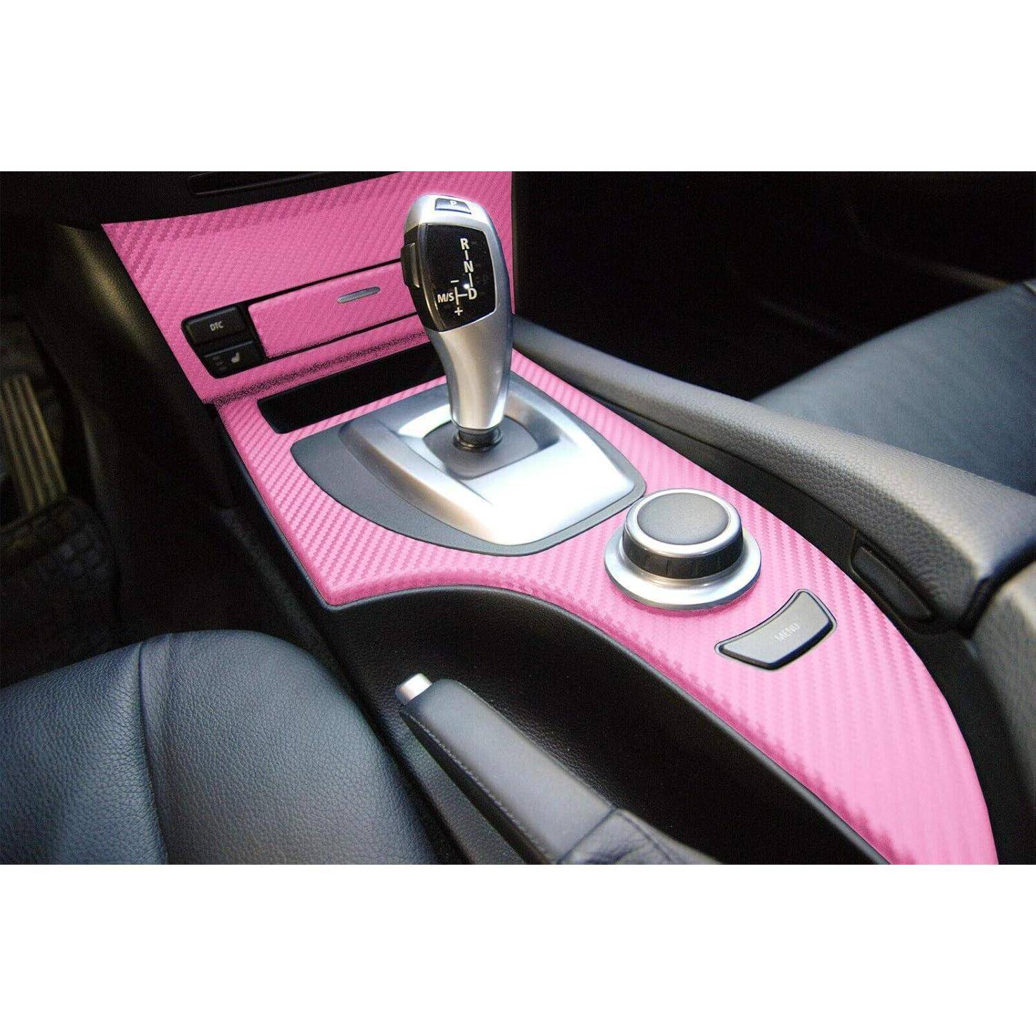 Nahaufnahme einer Mittelkonsole eines Autos mit einer rosa Kohlefaser-Verkleidung, automatischer Gangschaltung und rundem Bedienknopf zwischen schwarzen Ledersitzen.