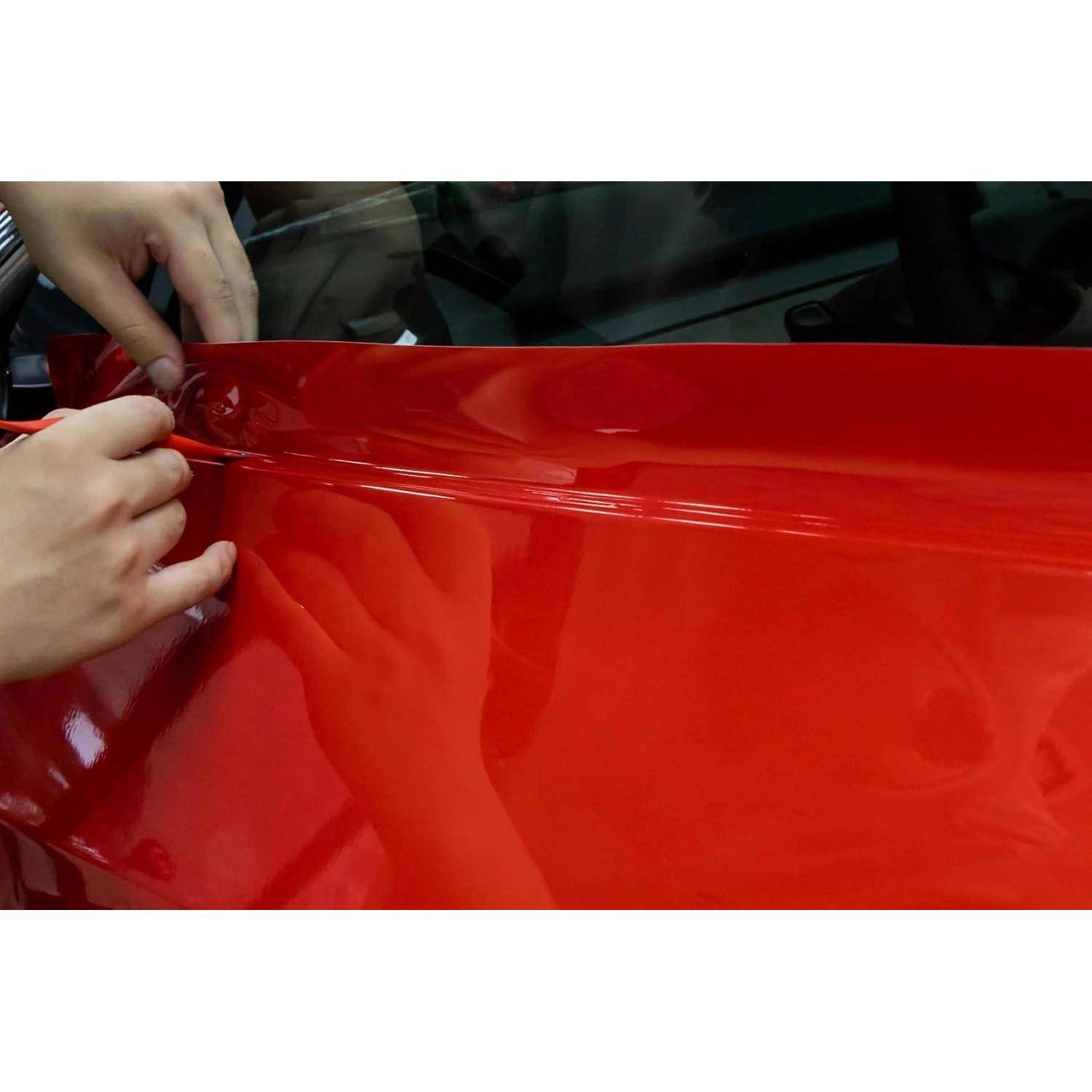 Hände, die rote Vinyl-Folie auf ein Autopanel auftragen, den Film glattstreichen und ausrichten.