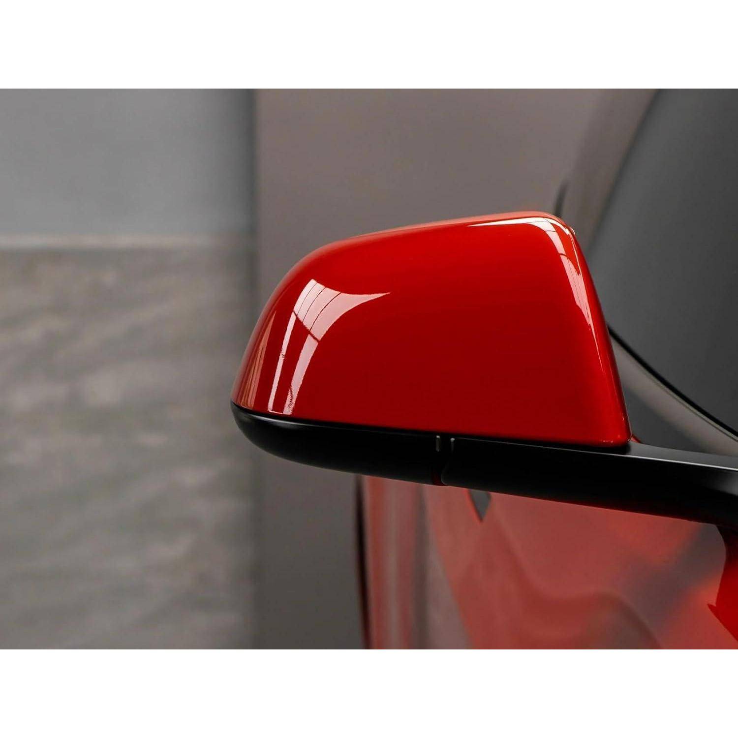 Nahaufnahme eines roten Seitenpiegels eines Autos mit glänzend schwarzer Basis vor einem unscharfen grauen Hintergrund.