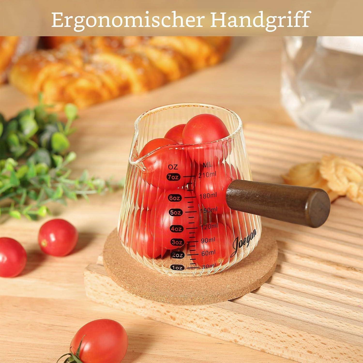 Glaskemesser mit Holzgriff und Ausguss, gefüllt mit Kirschtomaten auf einem Holztisch; Text lautet „Ergonomischer Handgriff