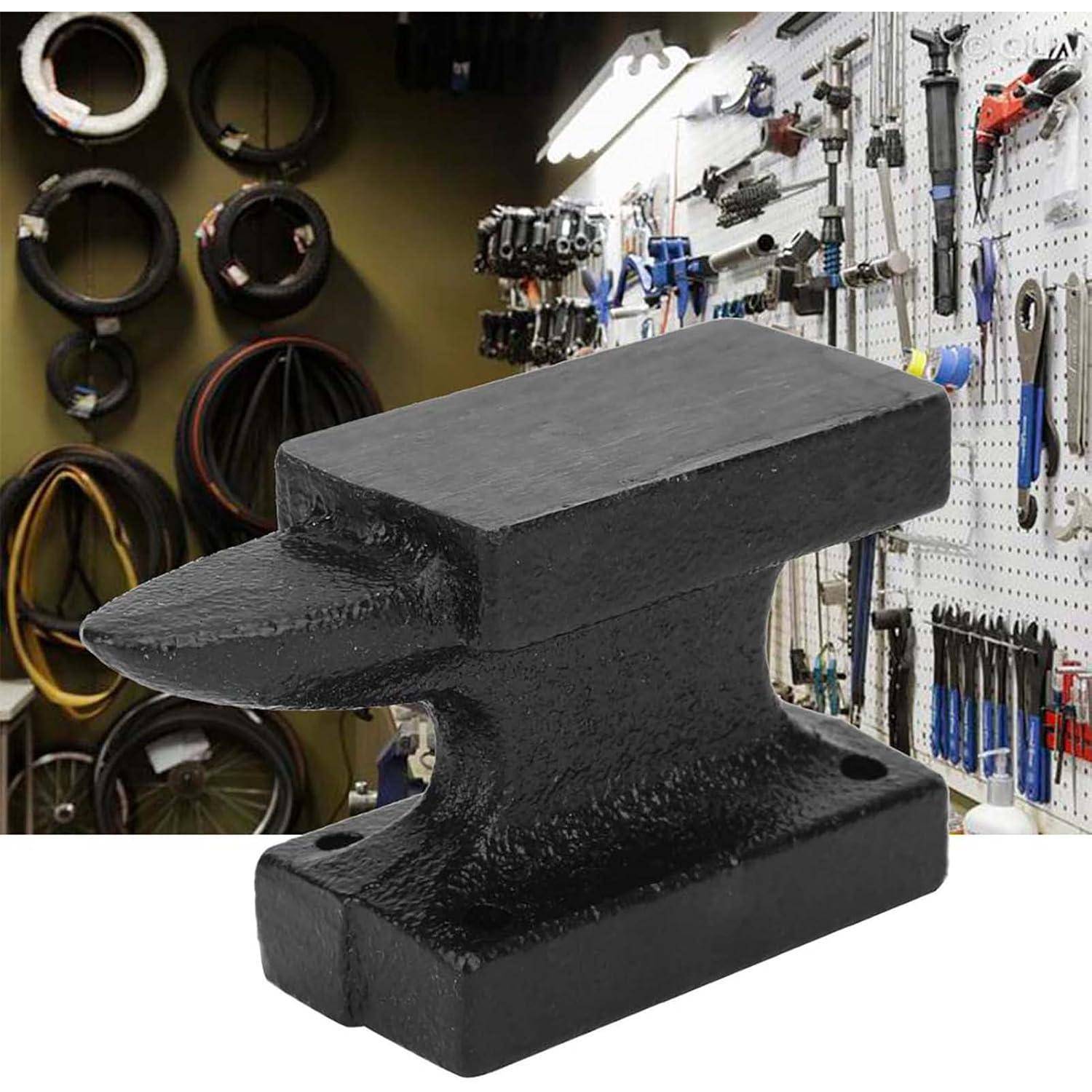 Schwarzer Amboss in einer Werkstatt, mit Werkzeugen und hängender Ausrüstung im Hintergrund sichtbar.