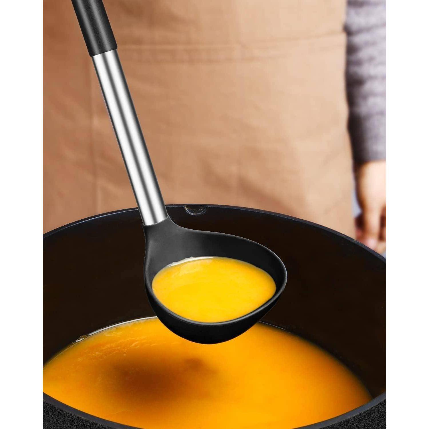 Schöpfkelle hebt leuchtend orangenfarbene Suppe aus einem großen schwarzen Topf, mit einer Person dahinter in der Küche stehend.