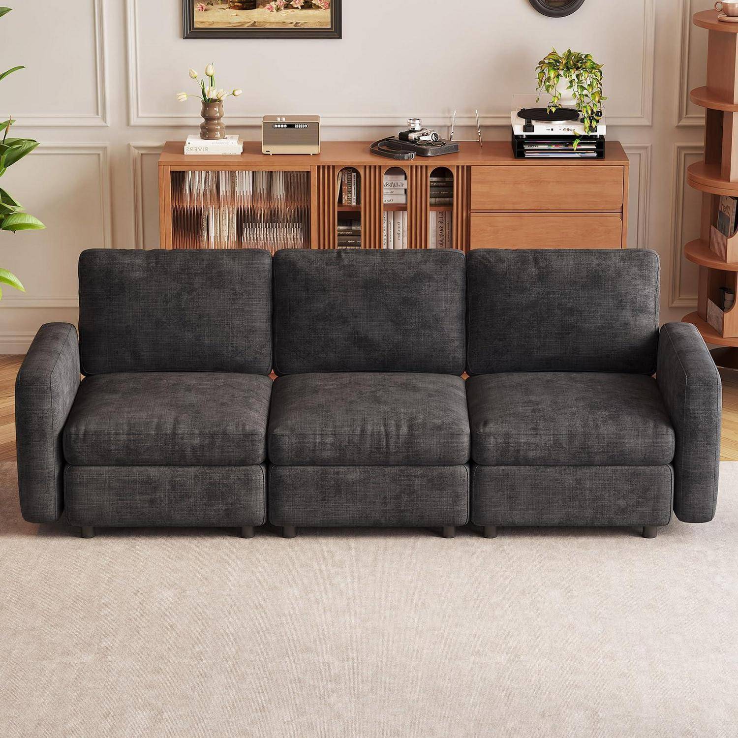 Dunkelgraues Dreisitzer-Sofa in einem Wohnzimmer mit hölzernem Sideboard und Pflanzen dahinter.