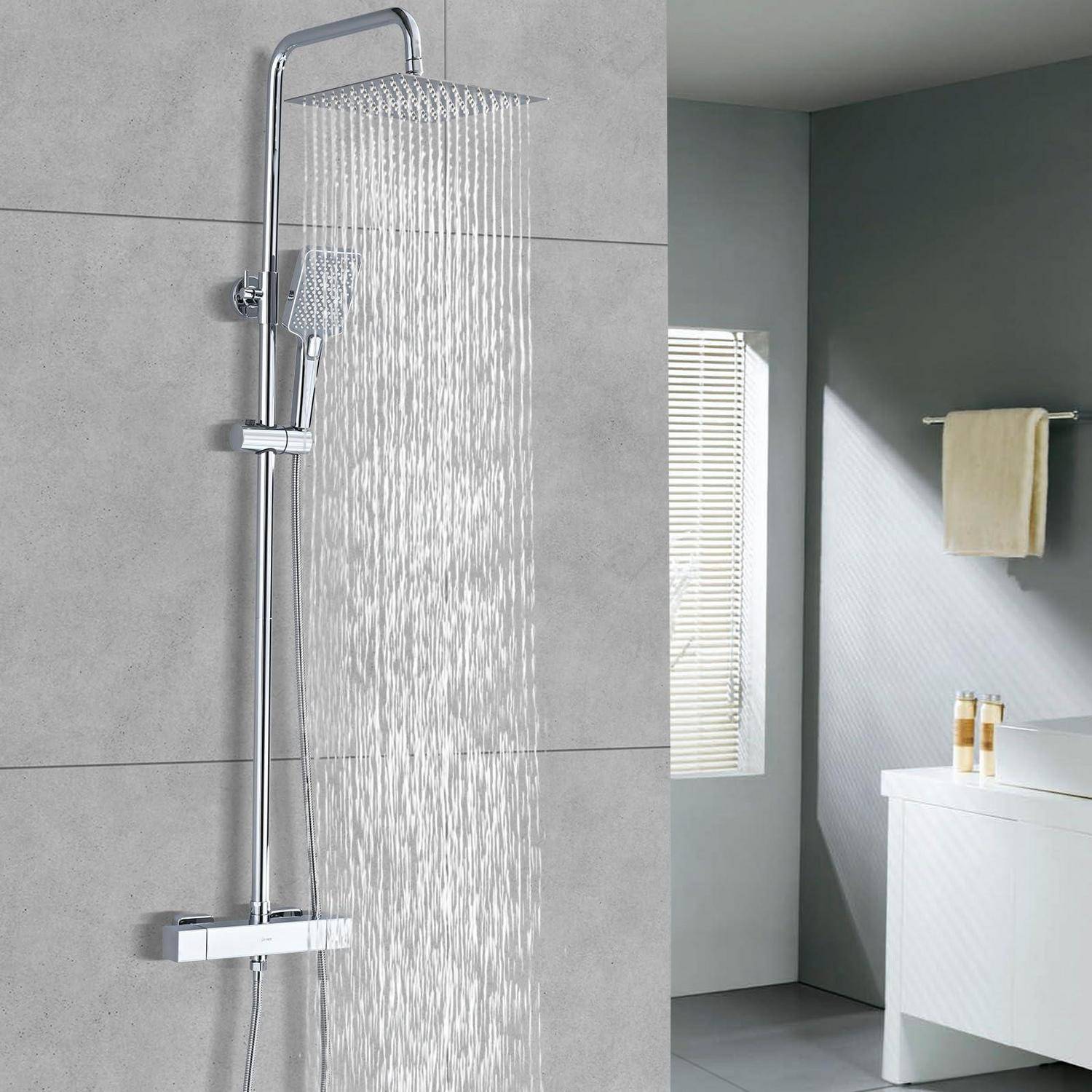 Modernes Badezimmer mit großem verchromtem Regenbrausenkopf, der Wasser neben einem Waschtisch, einem Handtuch und einem Fenster mit Jalousien sprüht.