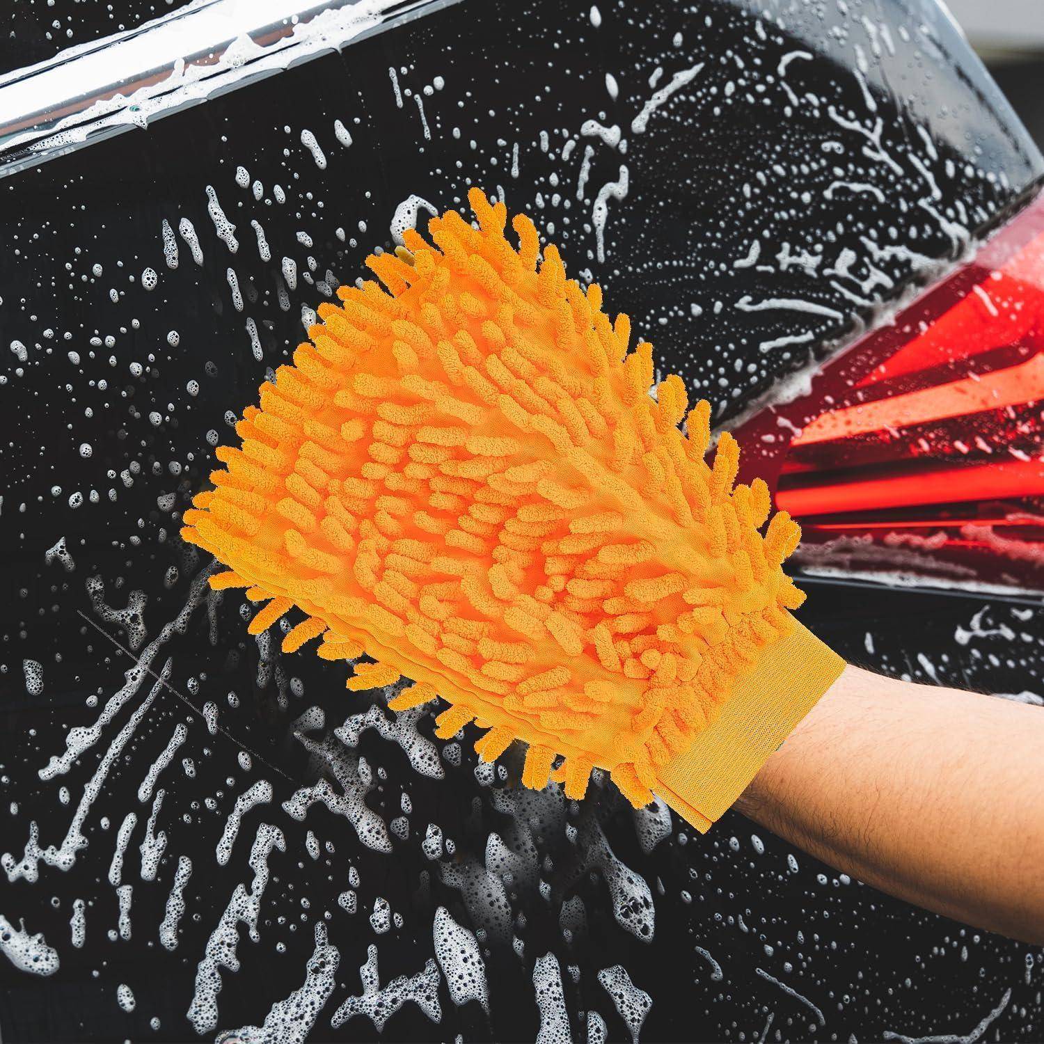 Eine leuchtend orangefarbene Mikrofaser-Waschhandschuh schrubbt ein schäumendes schwarzes Autofenster während des Autowaschen.