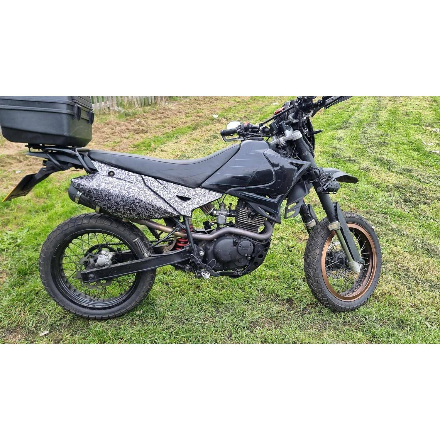 Schwarzes Dual-Sport-Motorrad auf Gras geparkt, Seitenansicht, mit hinterer Ladebox und Stollenreifen.