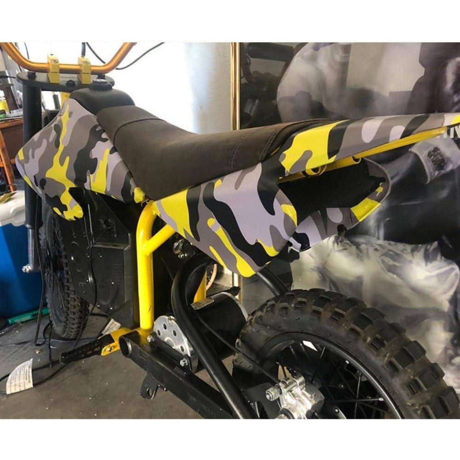 Getarnte Gelände-Dirt-Bike mit schwarzem Sitz und gelbem Rahmen, von hinten in Innenräumen fotografiert.