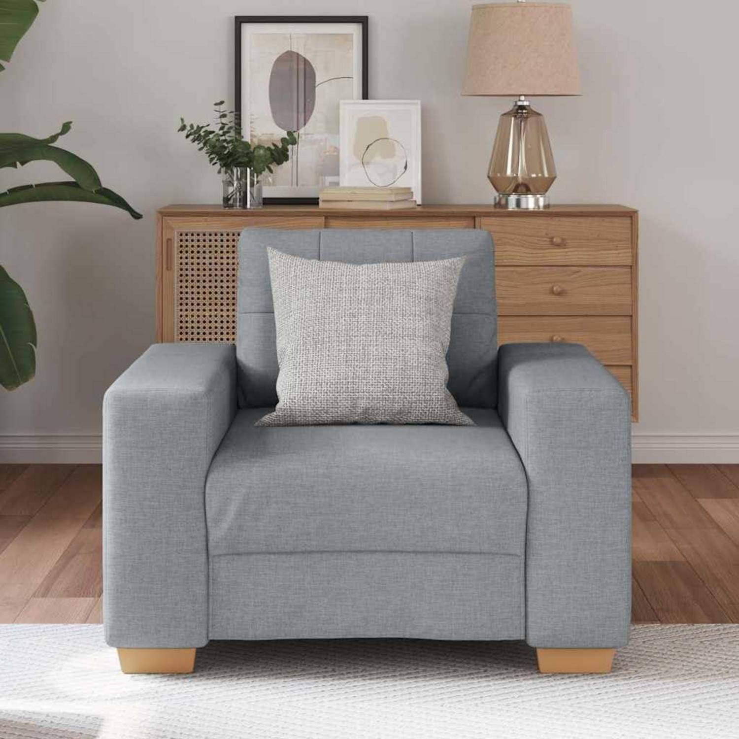 Hellblauer Sessel mit leichtem Kissen in einem modernen Wohnzimmer, vor einem Holz-Sideboard mit Lampe, Pflanzen und gerahmter Kunst.