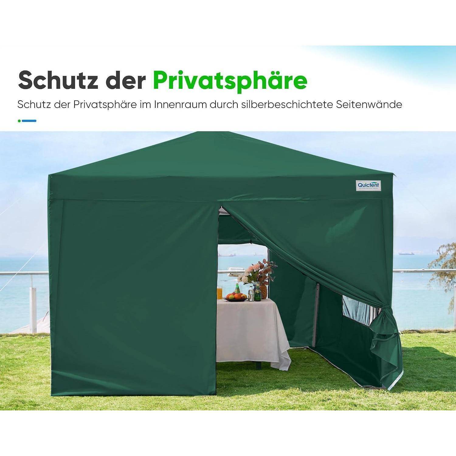 Grünes Datenschutzzelt mit silberausgekleideten Seitenwänden auf einem Rasen am Wasser, mit offenem Front und einem darin eingerichteten Tisch.