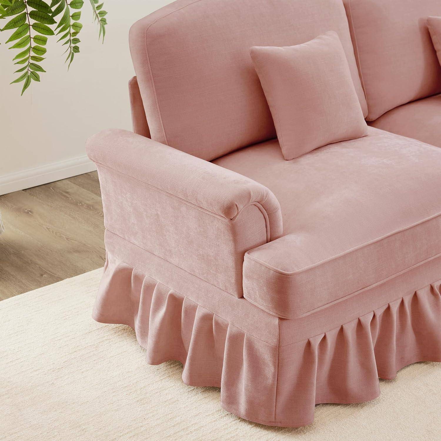 Rosa gepolstertes Sofa mit gekräuseltem Volant und passendem Kissen auf einem hellen Teppich in einem hellen Raum, mit einer belaubten Pflanze in der Nähe.