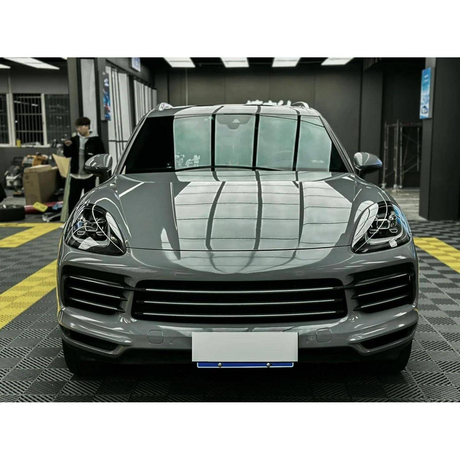Frontansicht eines grauen Porsche SUV, der drinnen geparkt ist, mit Blick auf den Kühlergrill, die Scheinwerfer und ein unscharfes Kennzeichen.