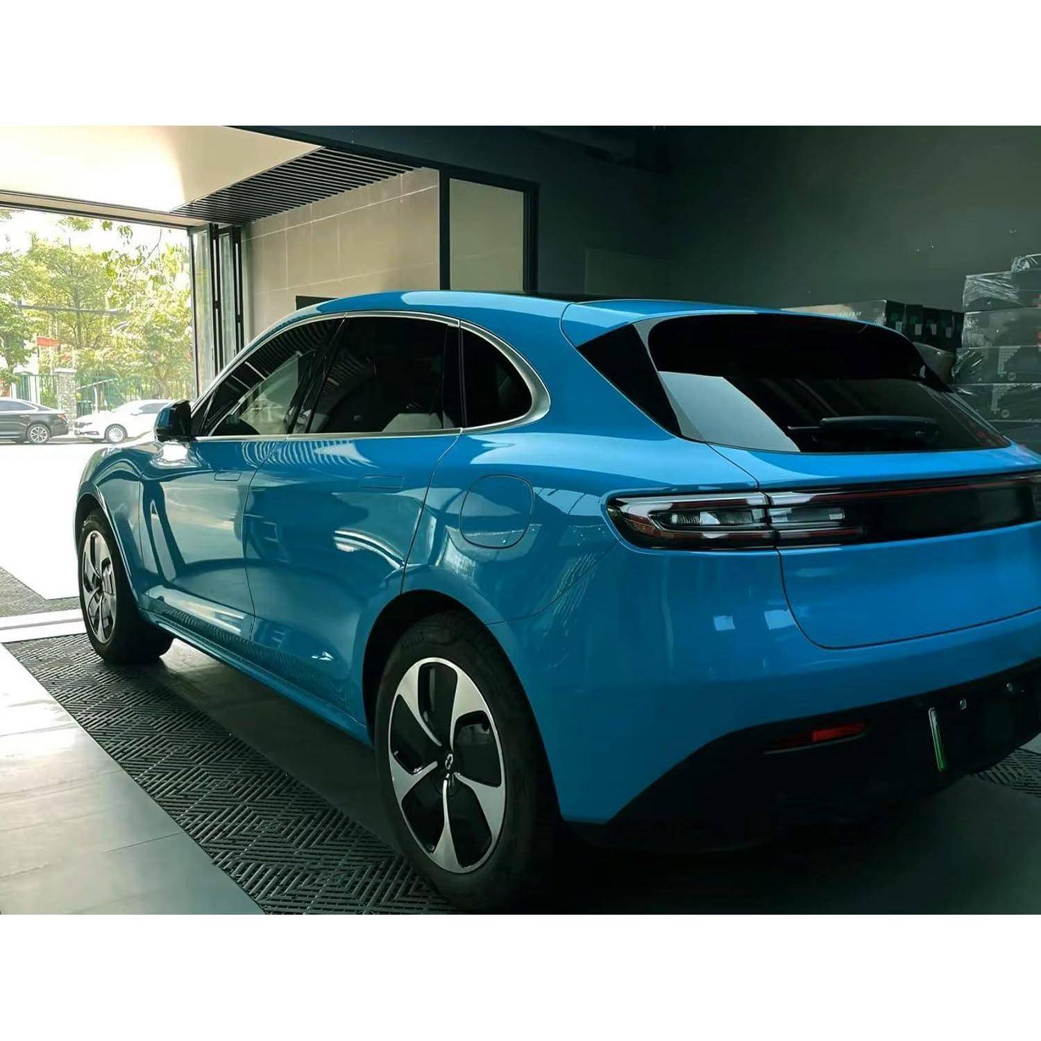 Blauer elektrischer SUV aus der hinteren linken Perspektive, geparkt in einem Innenbereich in der Nähe eines offenen Ausstellungsraum-Eingangs.