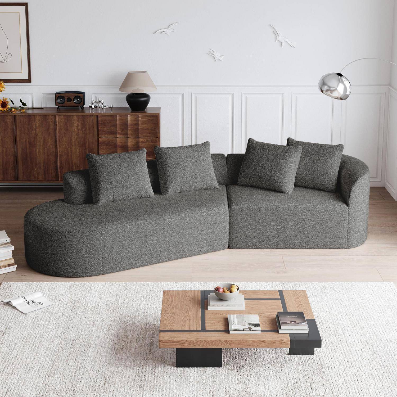 Modernes Wohnzimmer mit einem grauen gebogenen Ecksofa, hölzernem Couchtisch, Sideboard, Stehleuchte und einem hellen Teppich in einem minimalistischen Interieur.