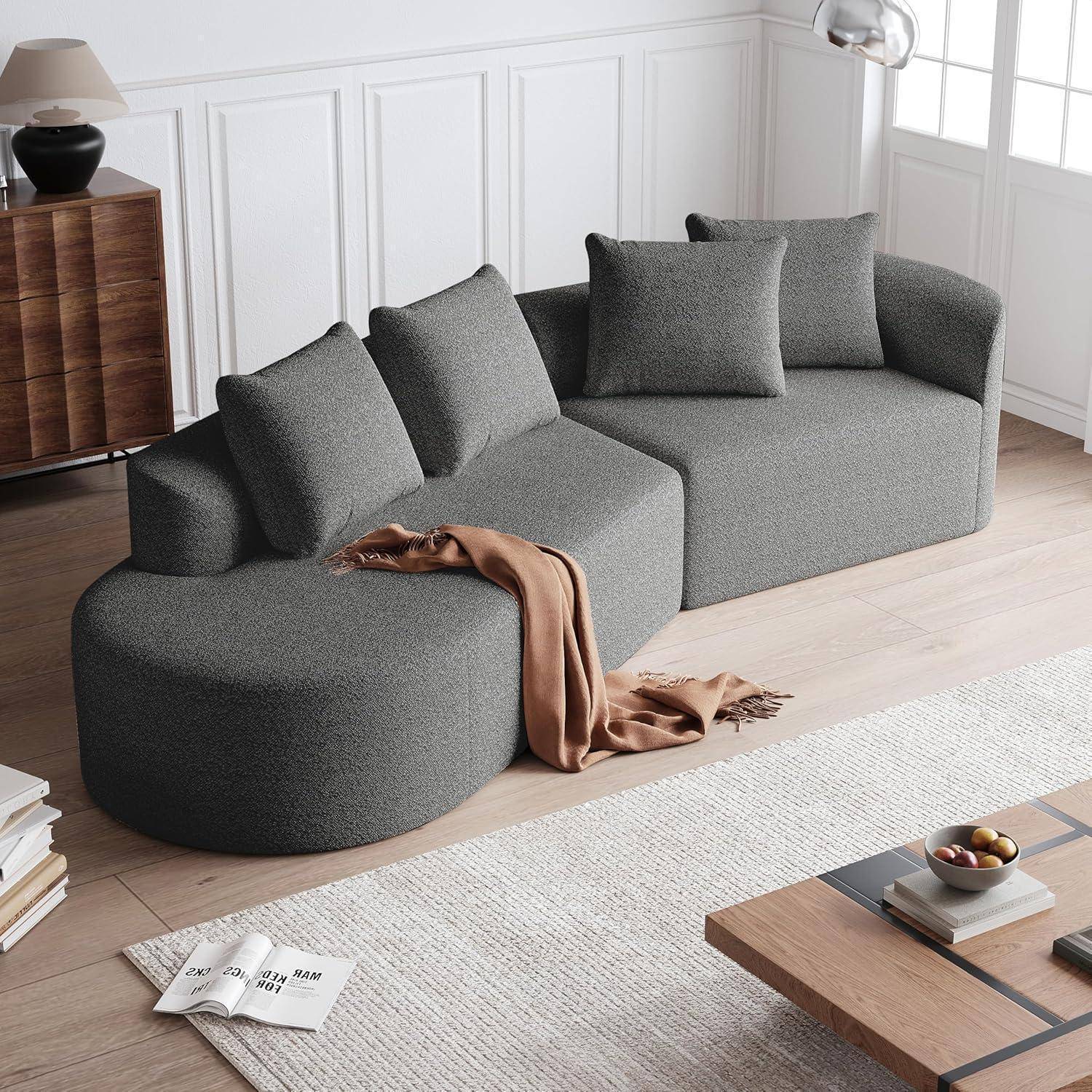 Modernes graues Ecksofa mit fünf Kissen und einer beigen Decke in einem hellen, minimalistischen Wohnzimmer.