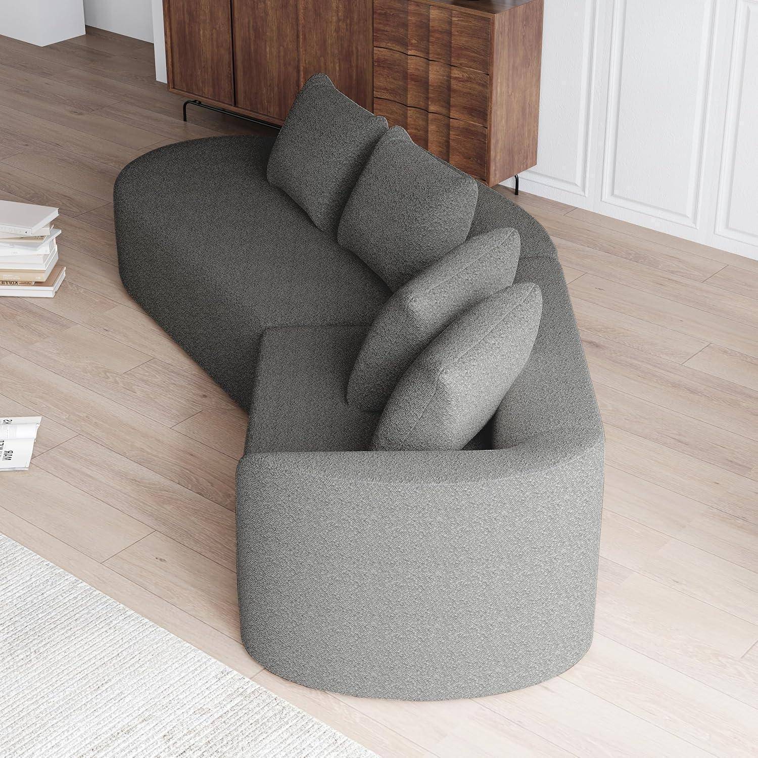 Grau geschwungenes Ecksofa mit drei Rückenkissen in einem modernen Raum mit Holzboden und Schrankwerk.