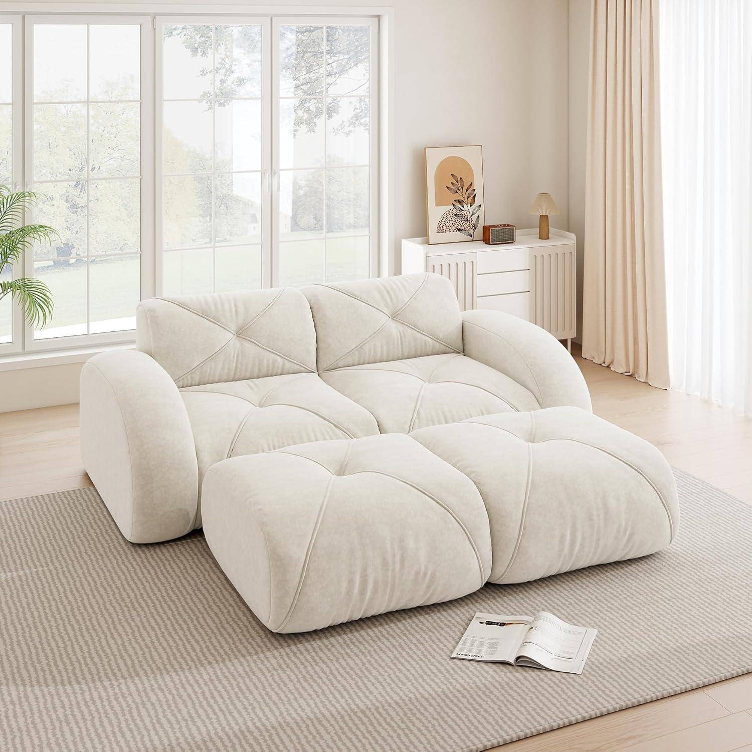 Ein cremefarbenes übergroßes gepolstertes Sofa sitzt in einem hellen, minimalistischen Wohnzimmer mit großen Fenstern, einem Teppich, einem Seitenschrank und einer offenen Zeitschrift.