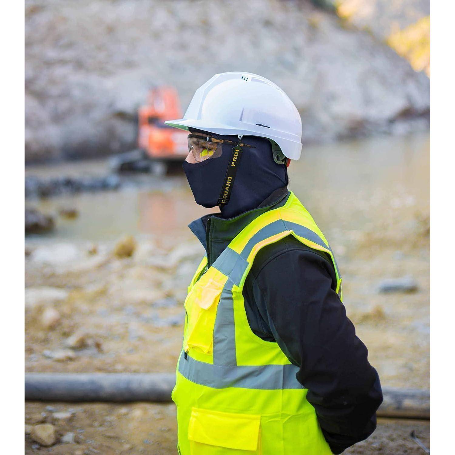 Bauarbeiter in einem Schutzhelm, einer Gesichtsmaske und einer Warnweste, der auf einer felsigen Baustelle steht.