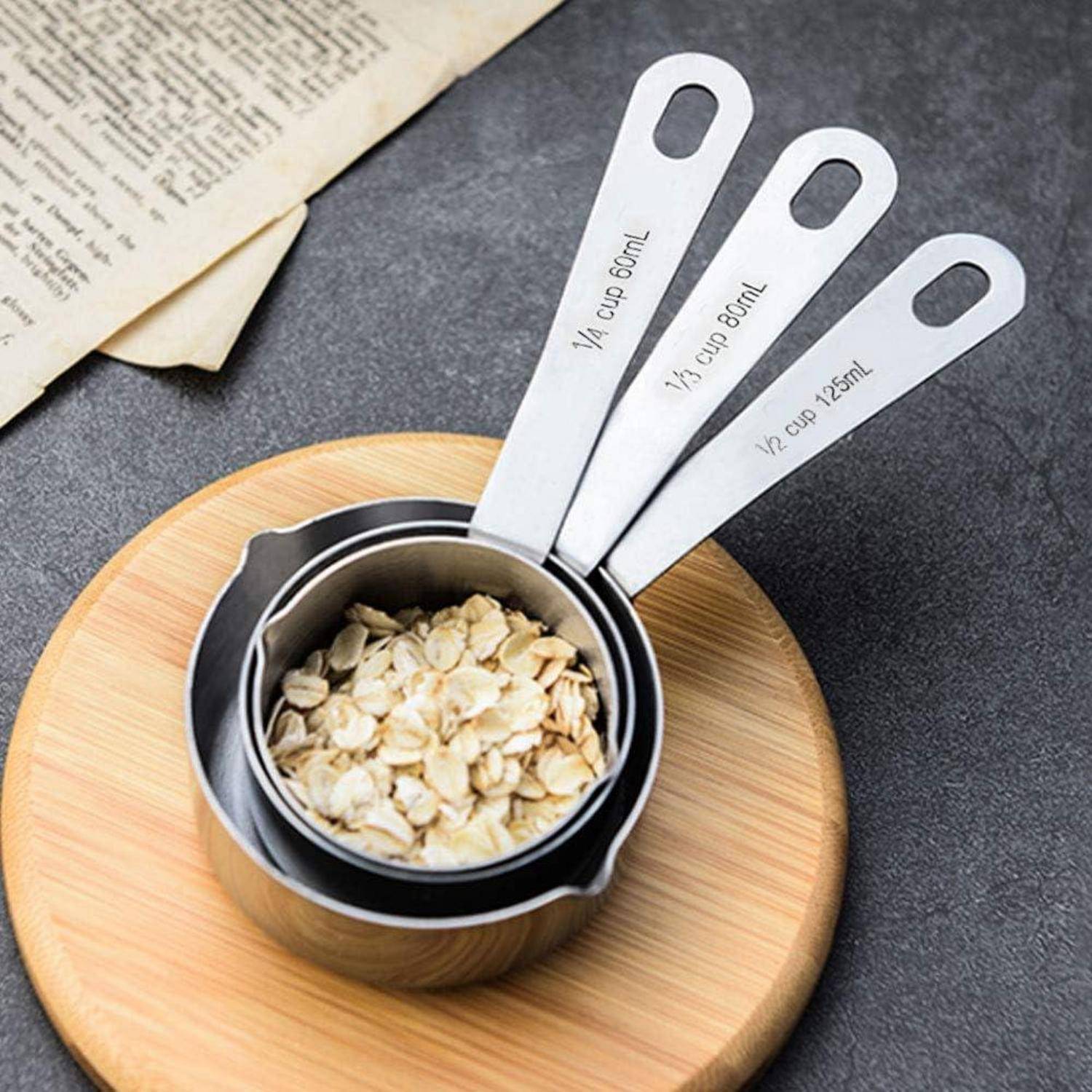 Messbehälter in einer Schüssel mit Haferflocken auf einem Holzbrett, mit Beschriftungen für 1/4 Tasse, 1/3 Tasse und 1/2 Tasse.