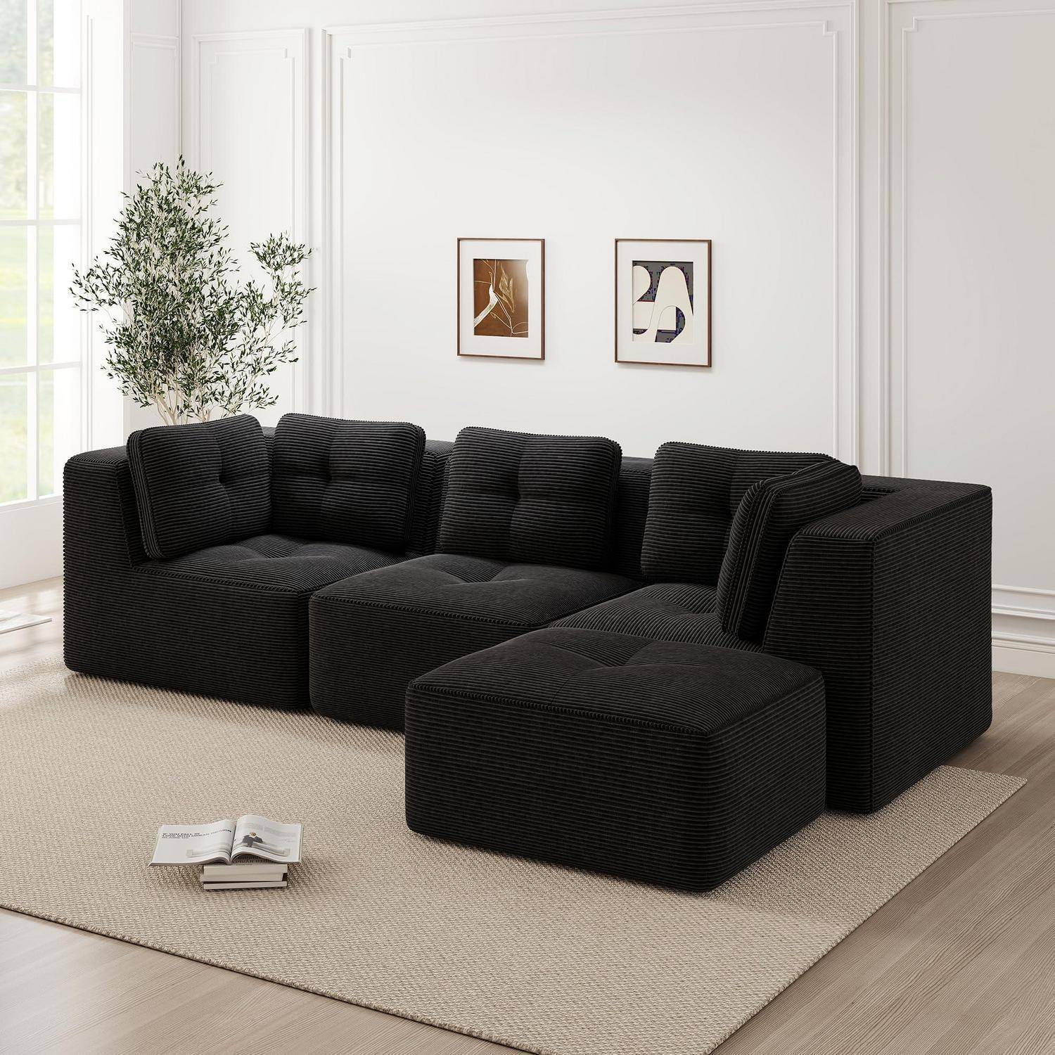 Schwarzes L-förmiges Ecksofa mit passendem Hocker auf einem beigen Teppich in einem hellen, minimalistischen Wohnzimmer, mit zwei gerahmten Drucken und einem Topfbaum.