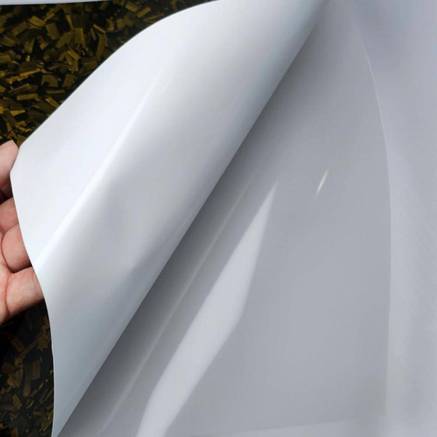 Eine Hand zieht ein leeres weißes Blatt oder eine Folie zurück und enthüllt eine glatte graue Oberfläche darunter.