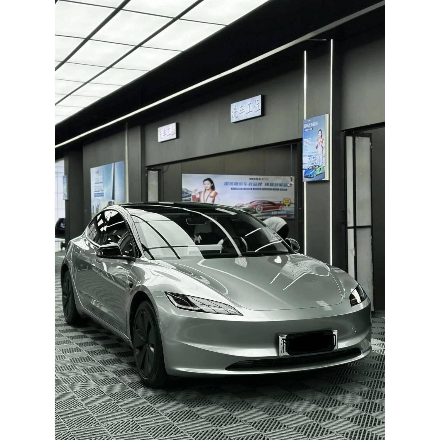 Silberner Tesla Model 3 Limousine in einem Showroom geparkt, Frontansicht auf gemustertem Boden mit Wandpostern dahinter.