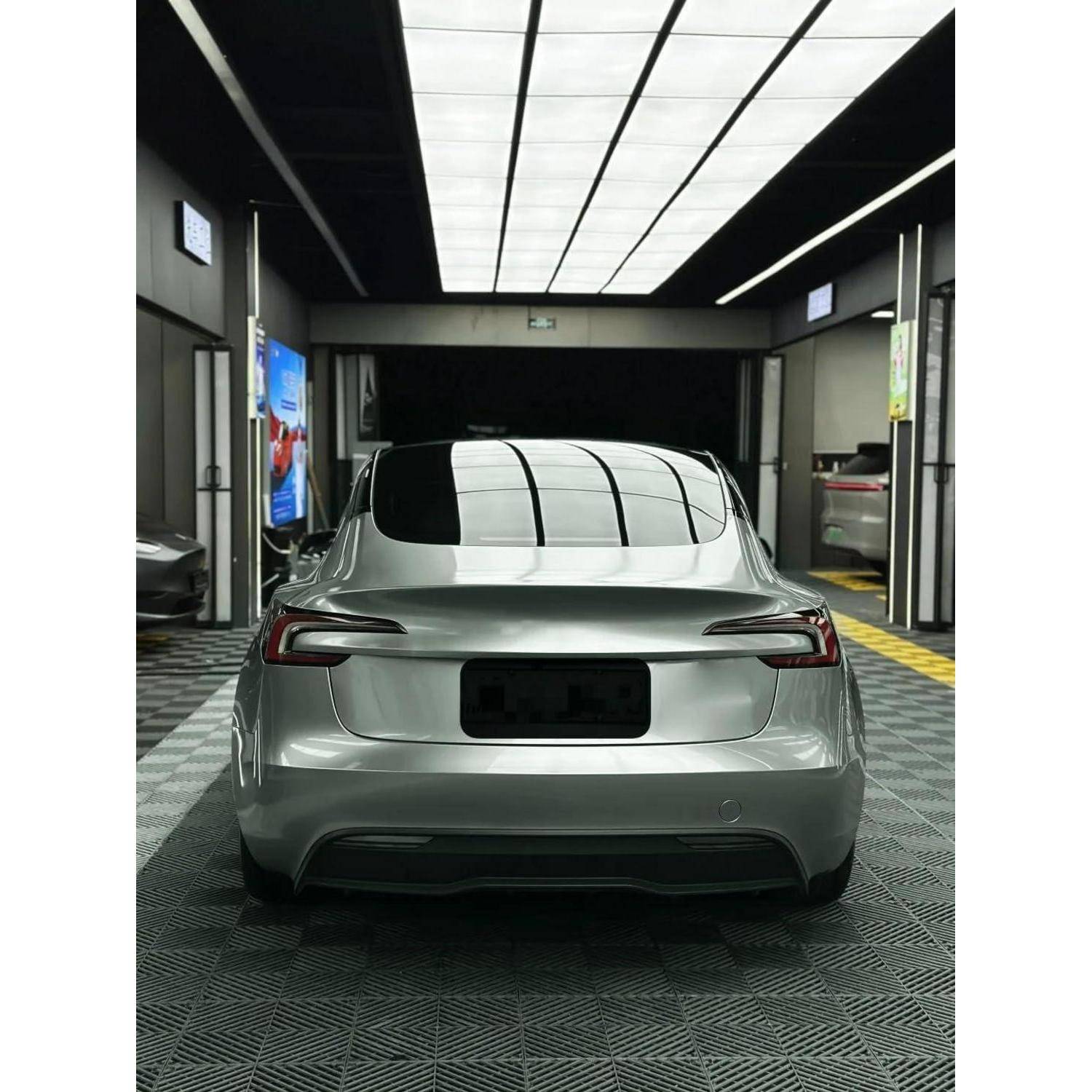 Heckansicht einer silbernen Tesla-Limousine, die in einer modernen Indoor-Garage oder Autowäsche-Box geparkt ist.