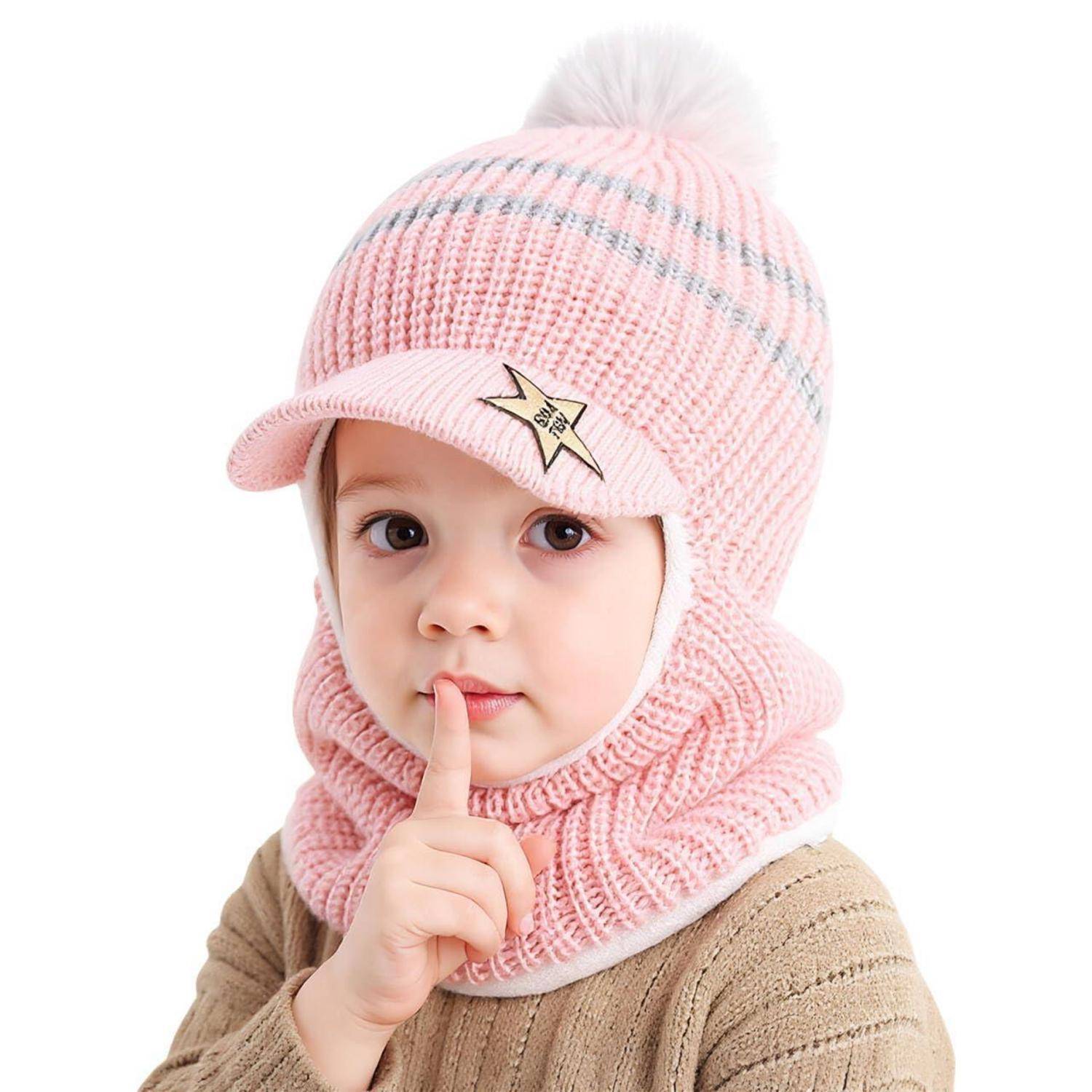 Kleines Kind mit einer rosa gestrickten Mütze und passendem Schal, das einen Finger an die Lippen hält in einer 