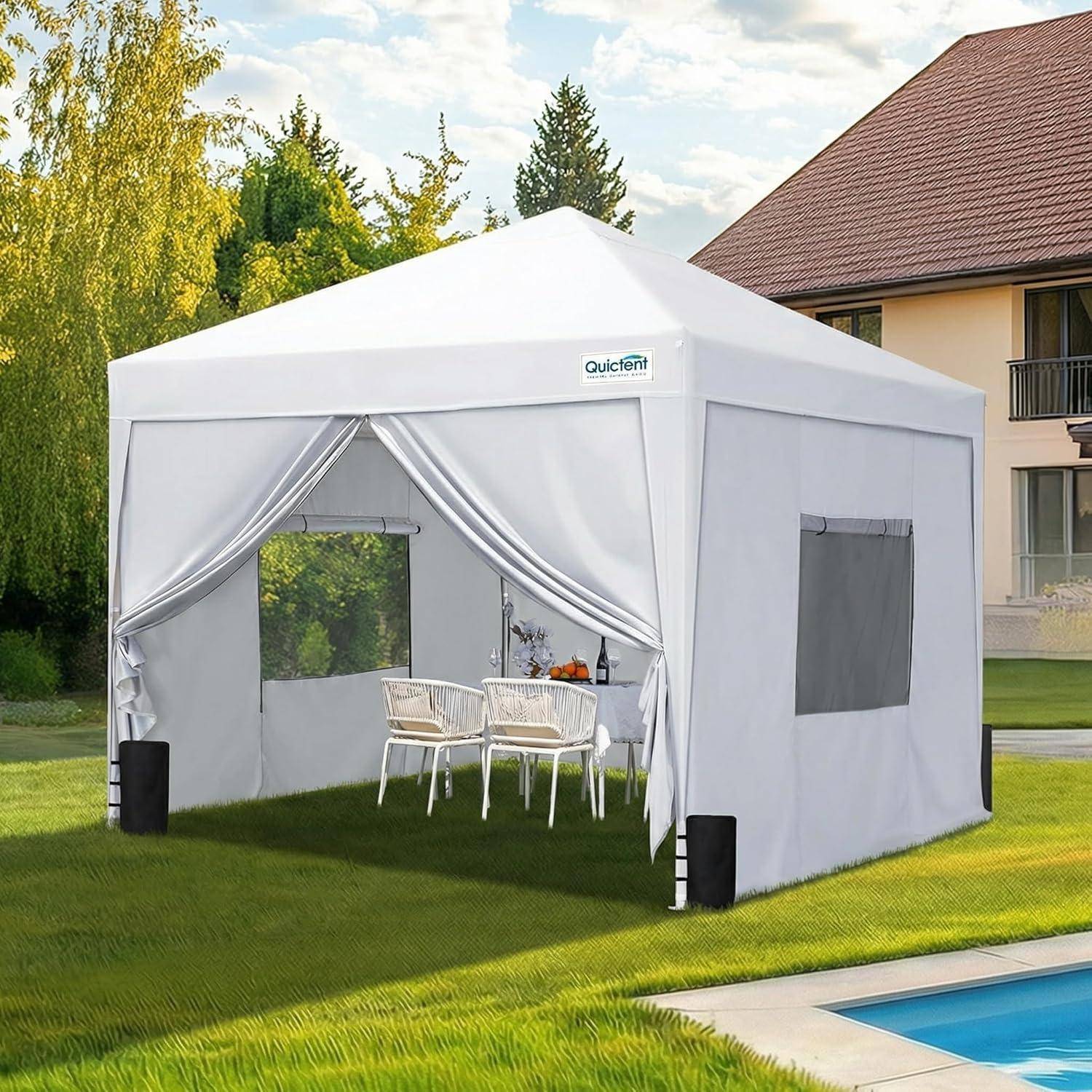 Weißes Gartenzelt mit offener Vorderseite im Freien, mit Tisch und Stühlen im Inneren, auf einem Rasen neben einem Swimmingpool in der Nähe eines Hauses aufgestellt.