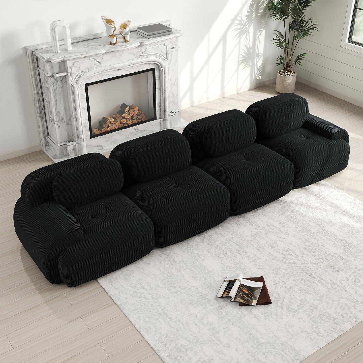 Schwarzes modulares Polstersofa in einem hellen Wohnzimmer mit weißem Kamin, hellem Teppich, Pflanze und Zeitschriften auf dem Boden.