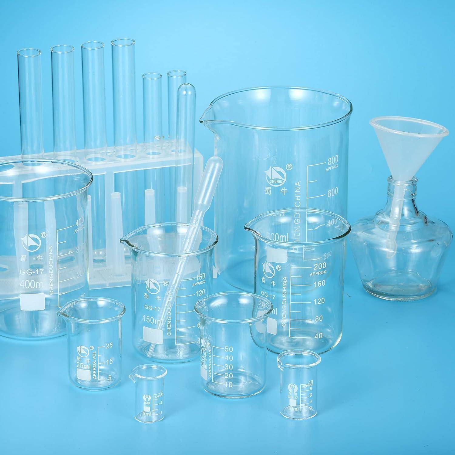 Glastropfen für Laborarbeiten, Reagenzgläser, Pipette, Trichter und kleine Fläschchen auf blauem Hintergrund angeordnet.