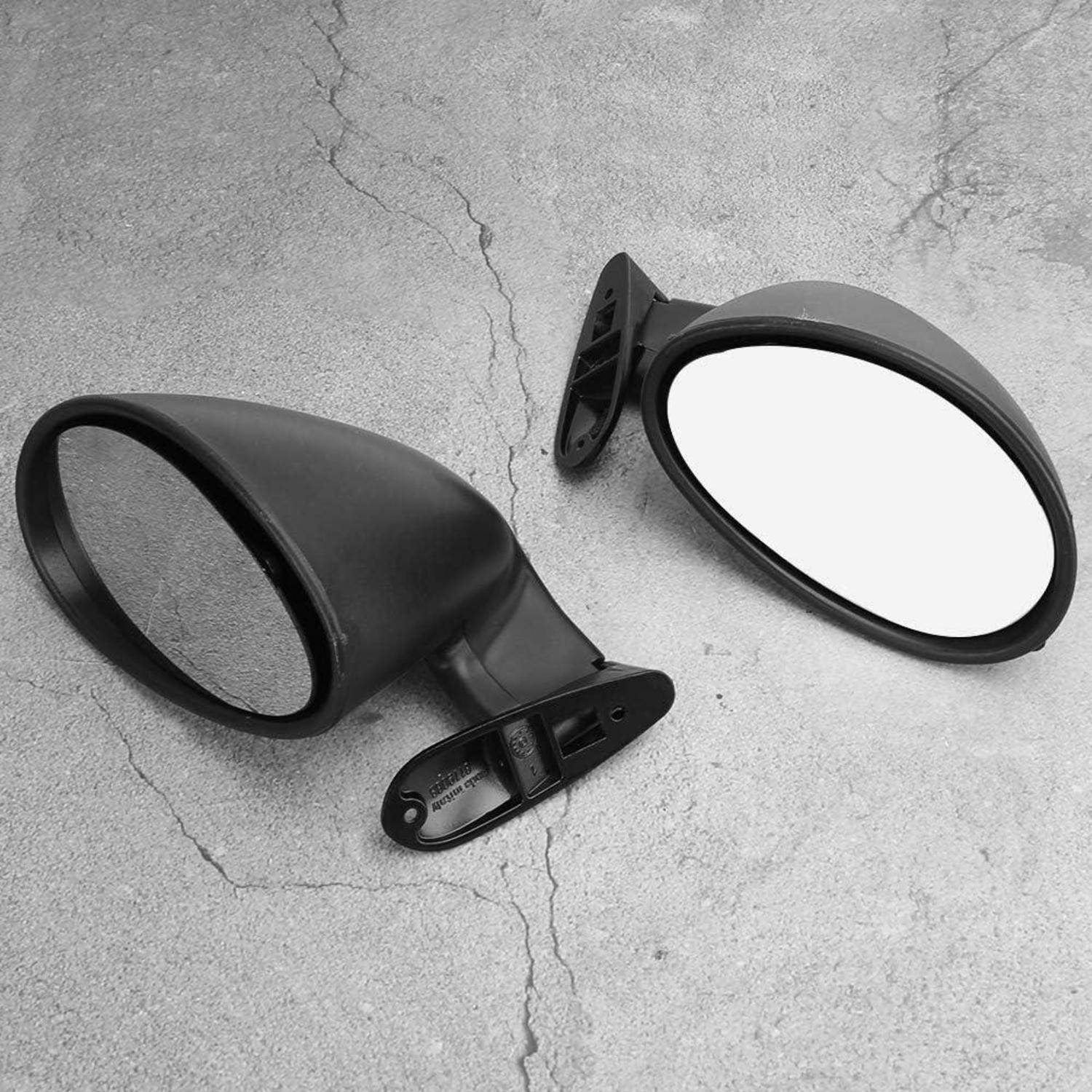 Zwei schwarze Außenspiegel eines Autos, einer zeigt die reflektierende Glasseite und einer die rückwärtige Gehäuseseite, liegen auf einer grauen Betonfläche.