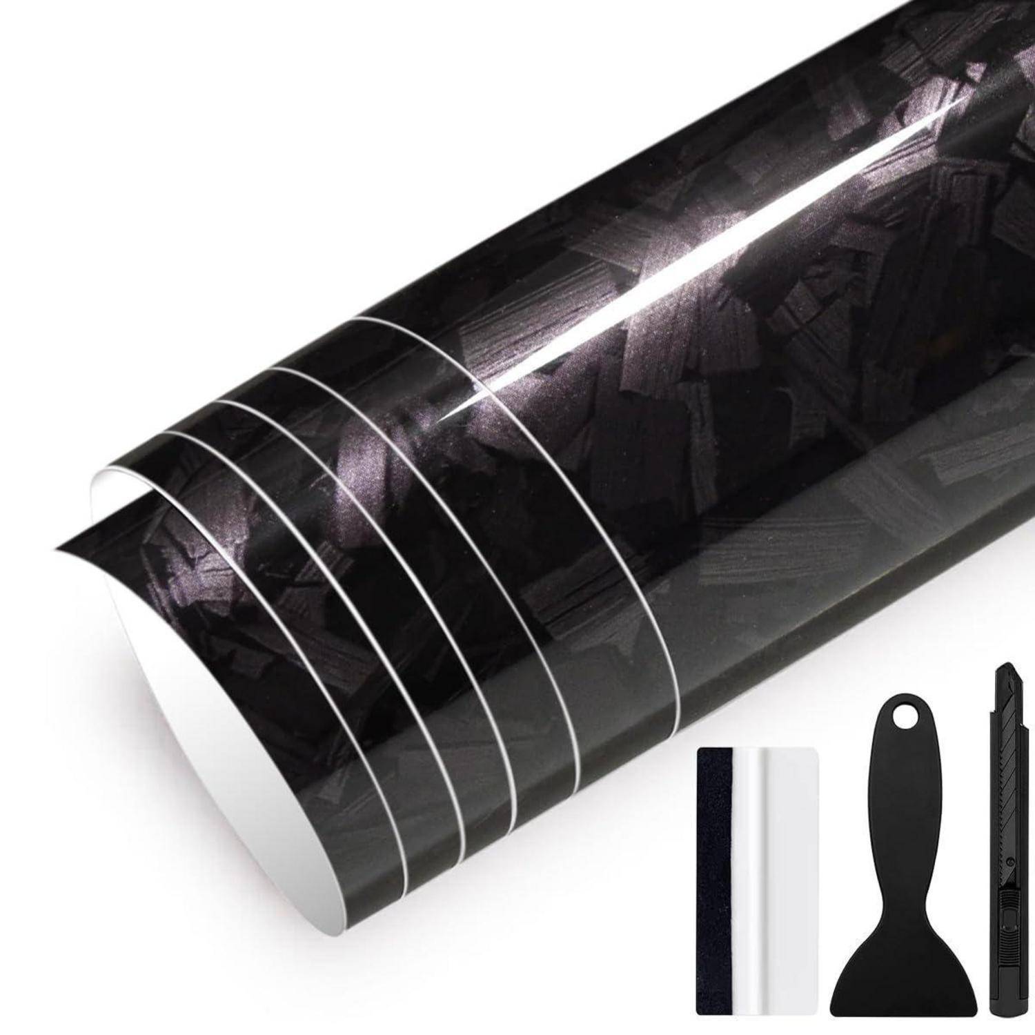 Rolle aus glänzendem schwarzem Kohlefaser-Vinyl mit weißen Ausrichtungslinien, gezeigt mit einem Rakel, Universalmesser und Musterstücken der Rückseite.