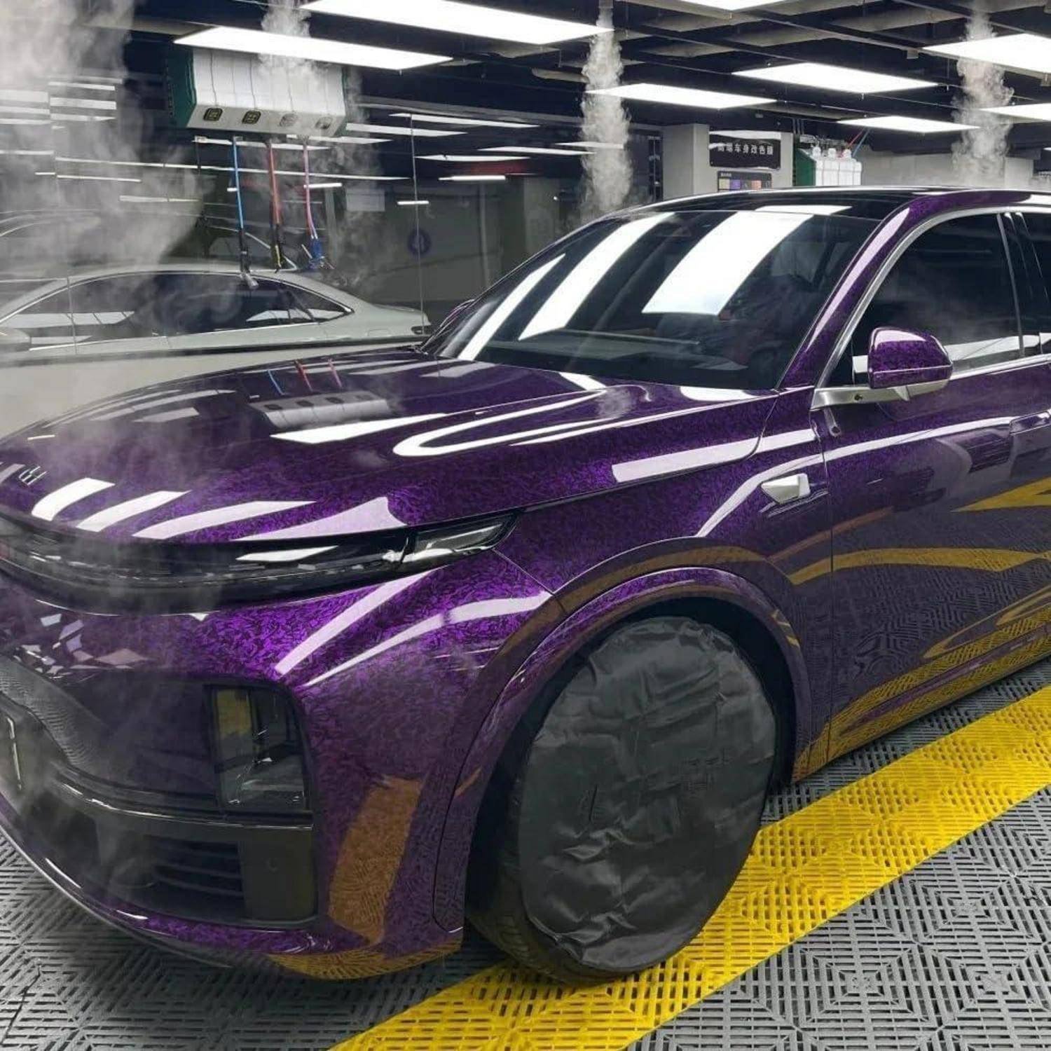 Violetter SUV mit glänzender, maßgeschneiderter Folierung, geparkt in einer Autowerkstatt im Innenbereich, mit abgedeckten Rädern und Reflexionen auf der Motorhaube.