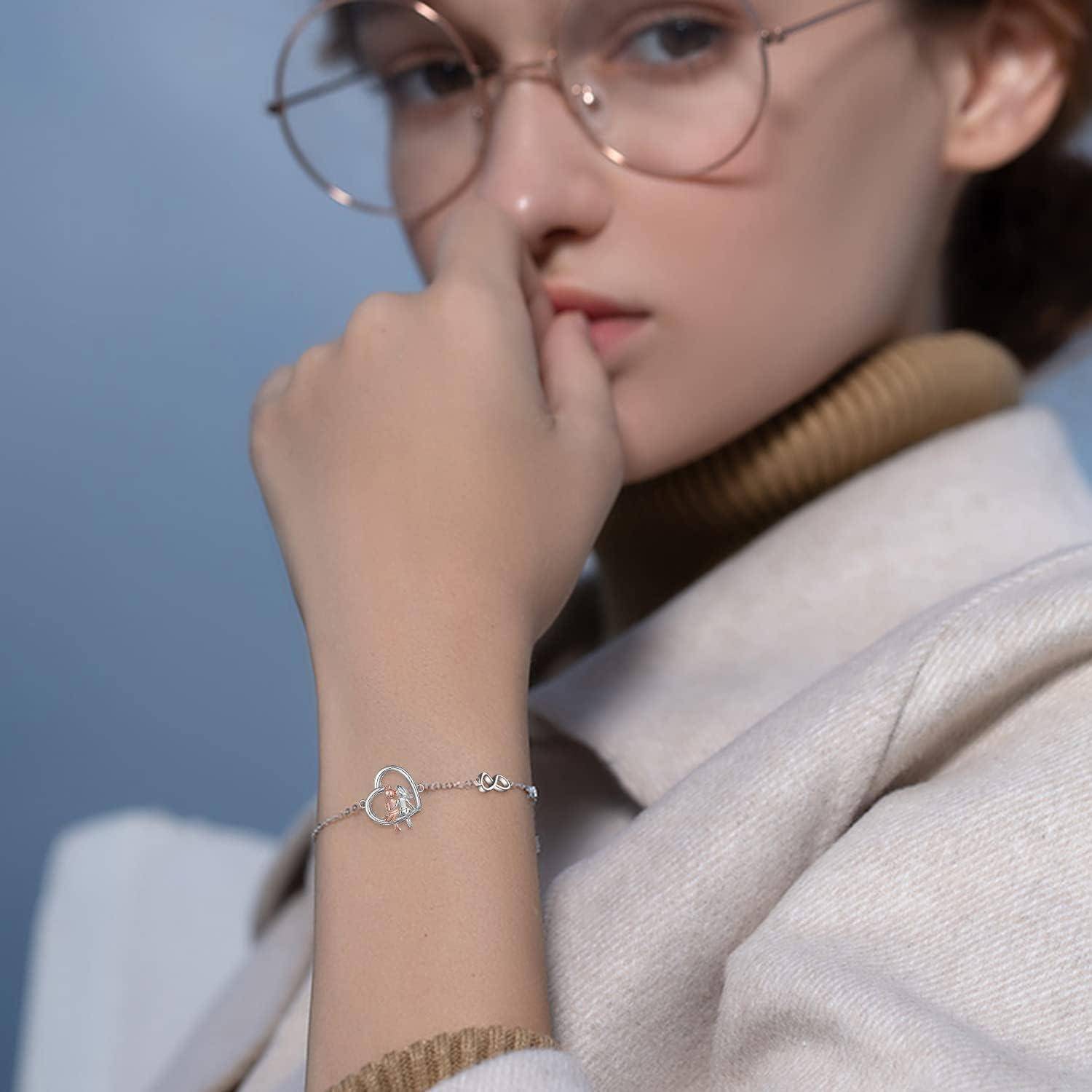 Nahaufnahme einer Frau, die eine Brille und ein herzförmiges Charm-Armband trägt, mit ihrer Hand, die sich neben ihrem Gesicht gegen einen blauen Hintergrund ruht.