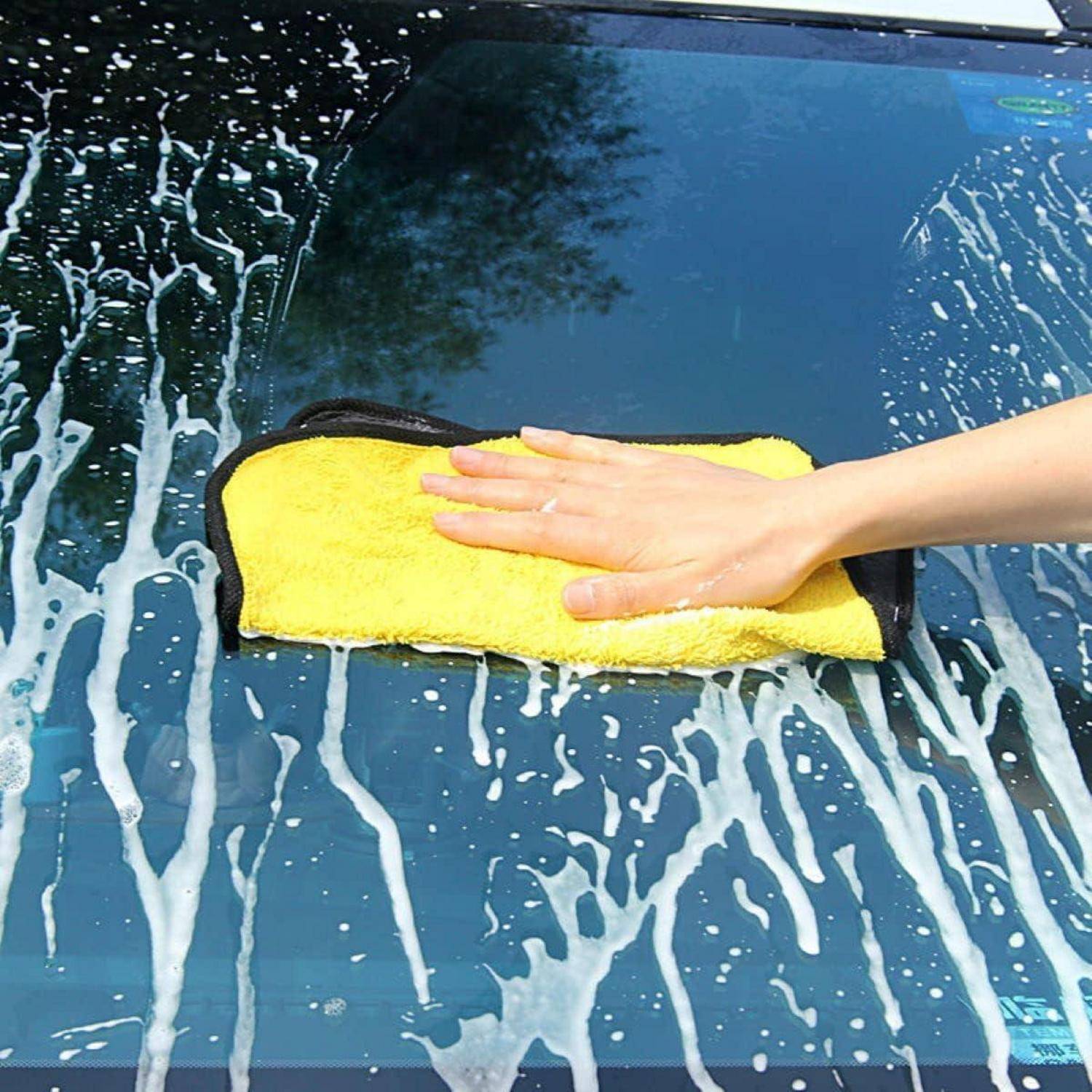 Hand wischt Seifenschaum mit einem gelben Schwamm oder Tuch von einer Autoscheibe ab.