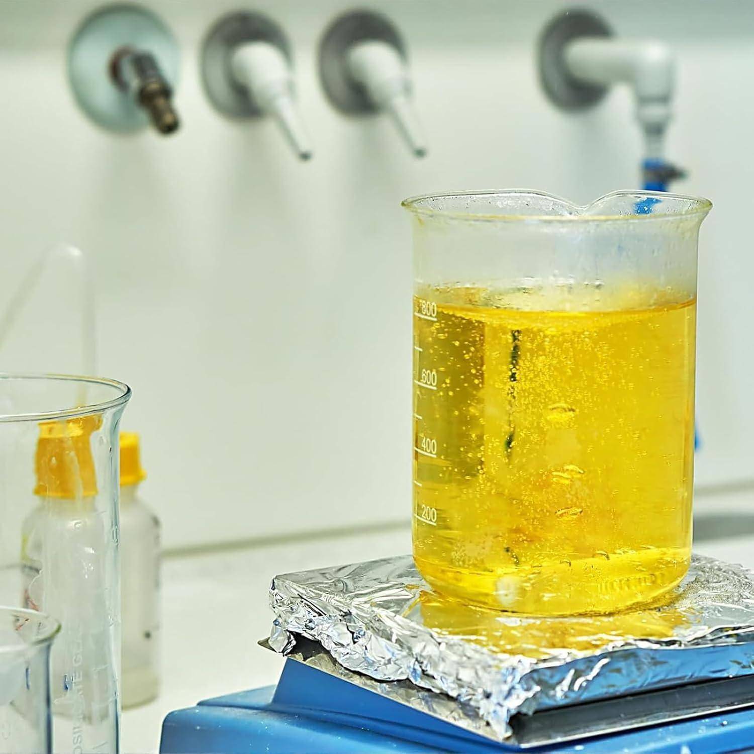 Becher mit gelber Flüssigkeit wird auf einer Laborbrennerplatte erhitzt, mit aufsteigenden Blasen in einem Chemielabor.