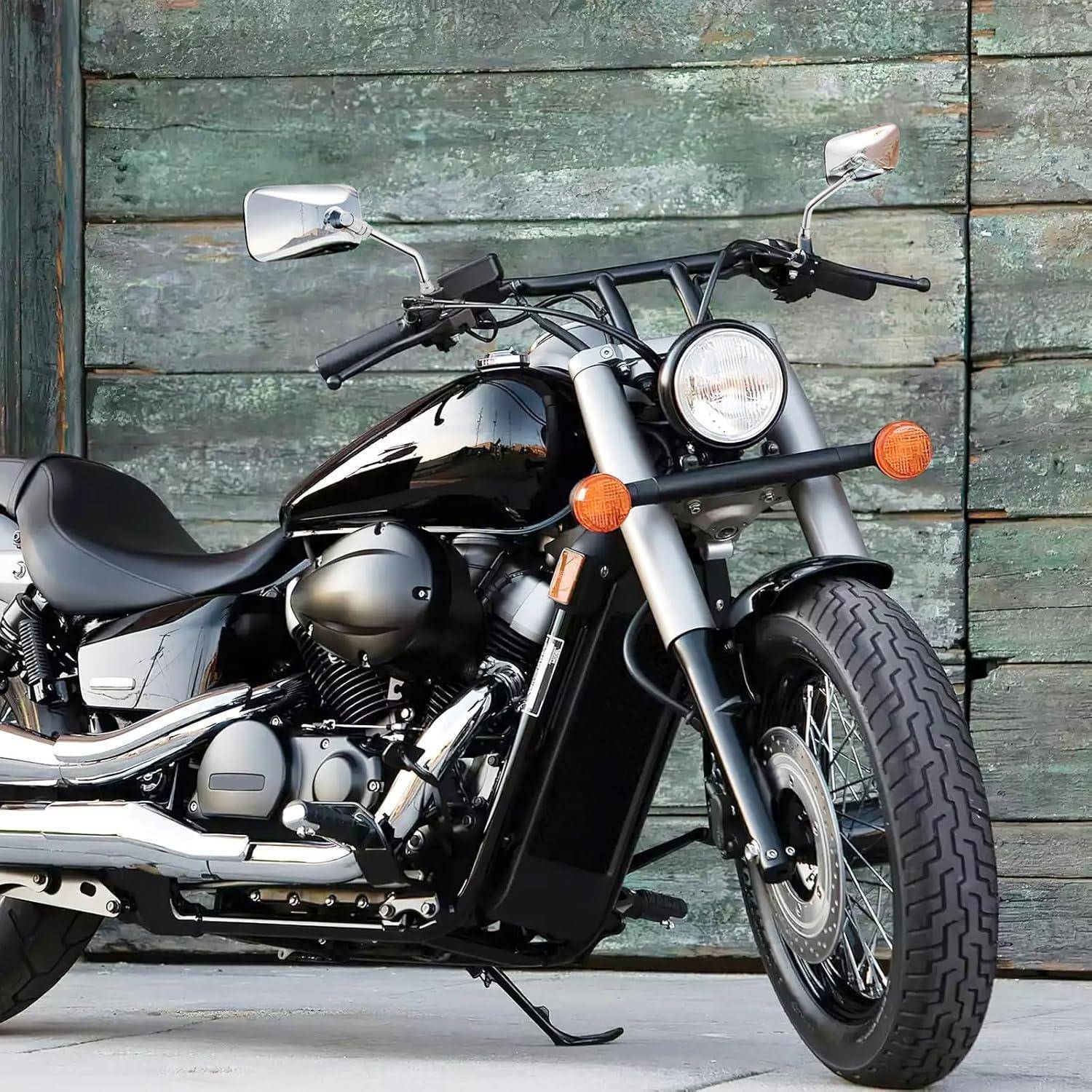 Schwarzes Cruiser-Motorrad geparkt auf einem Betonboden vor einer verwitterten grünen Holzwand.